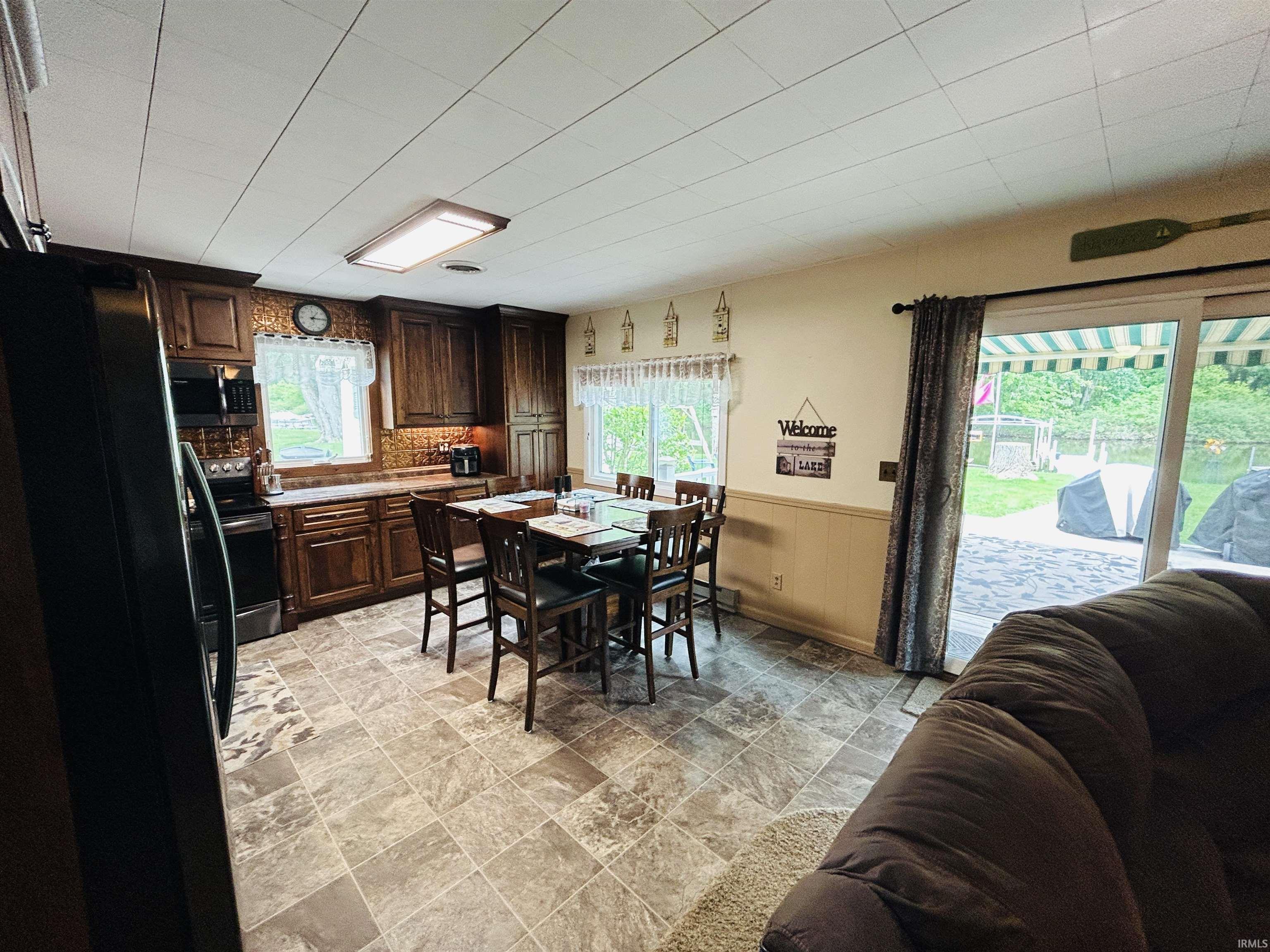 Kitchen area featuring wood cabinetry, integrated black appliances, and stone-look flooring