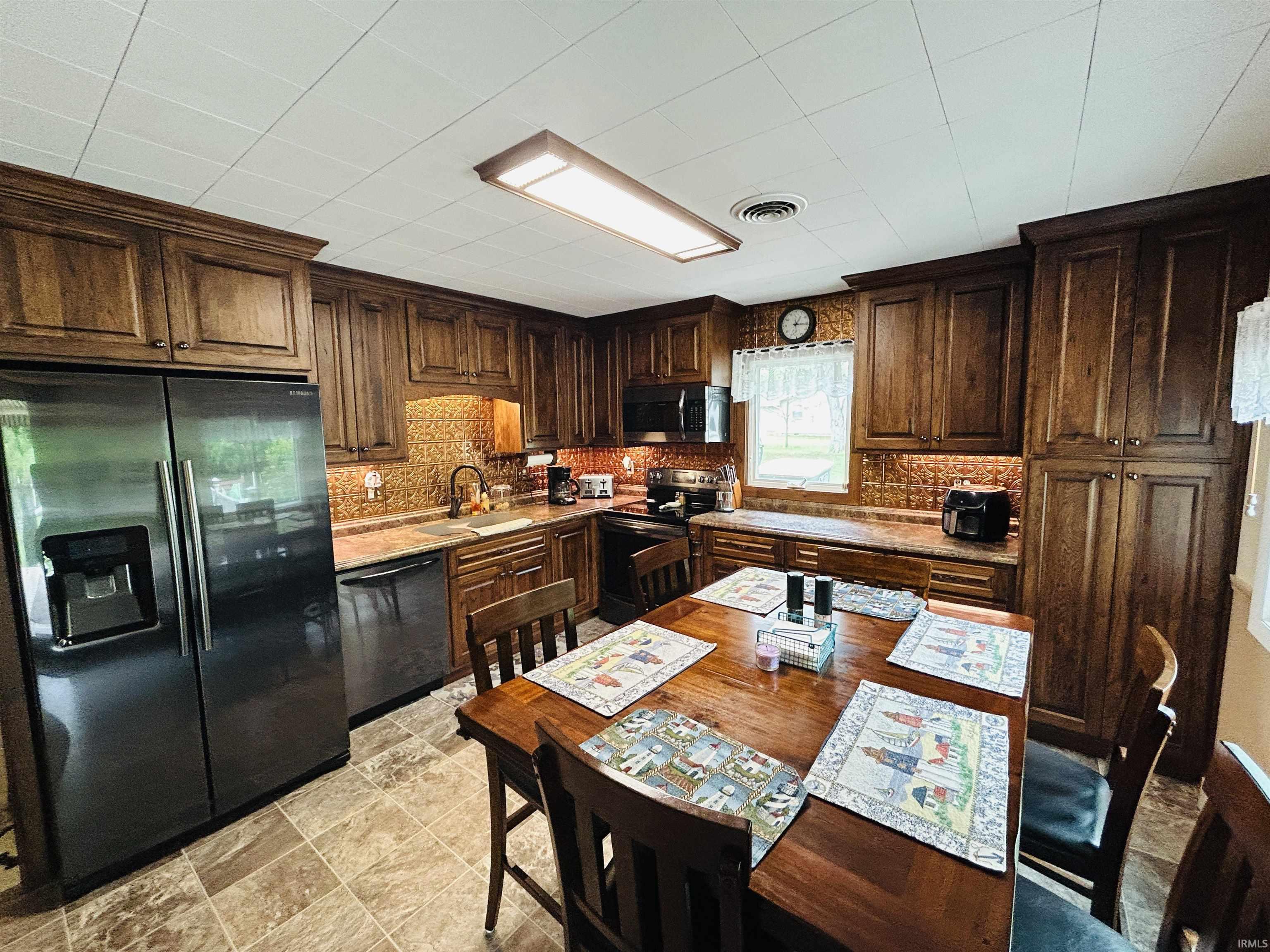 Kitchen featuring wood cabinetry, stainless steel appliances, a patterned tile backsplash, and stone-look flooring