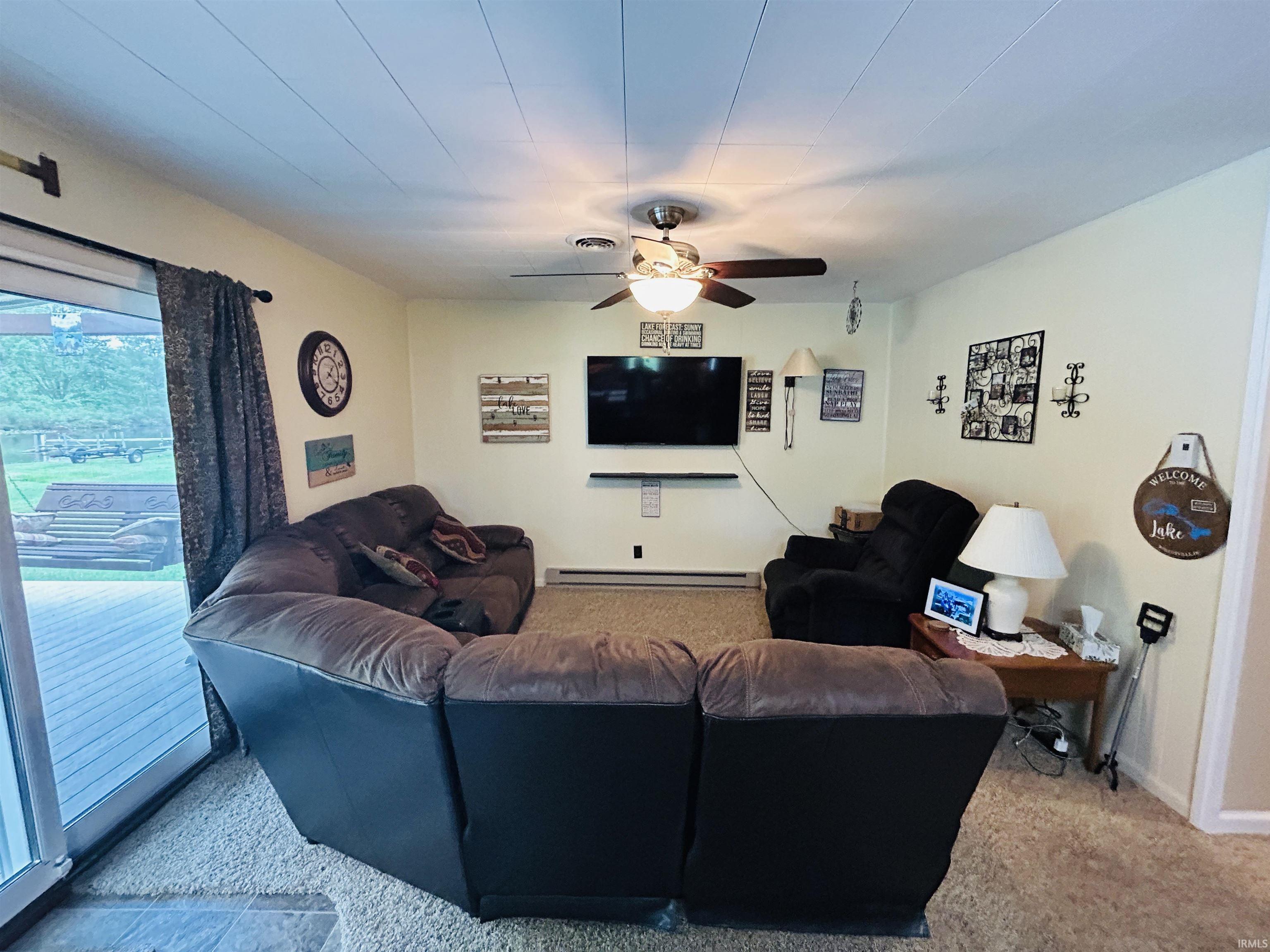 Carpeted living area featuring a ceiling fan with integrated lighting, light-toned wall paint, and a sliding glass door providing exterior access