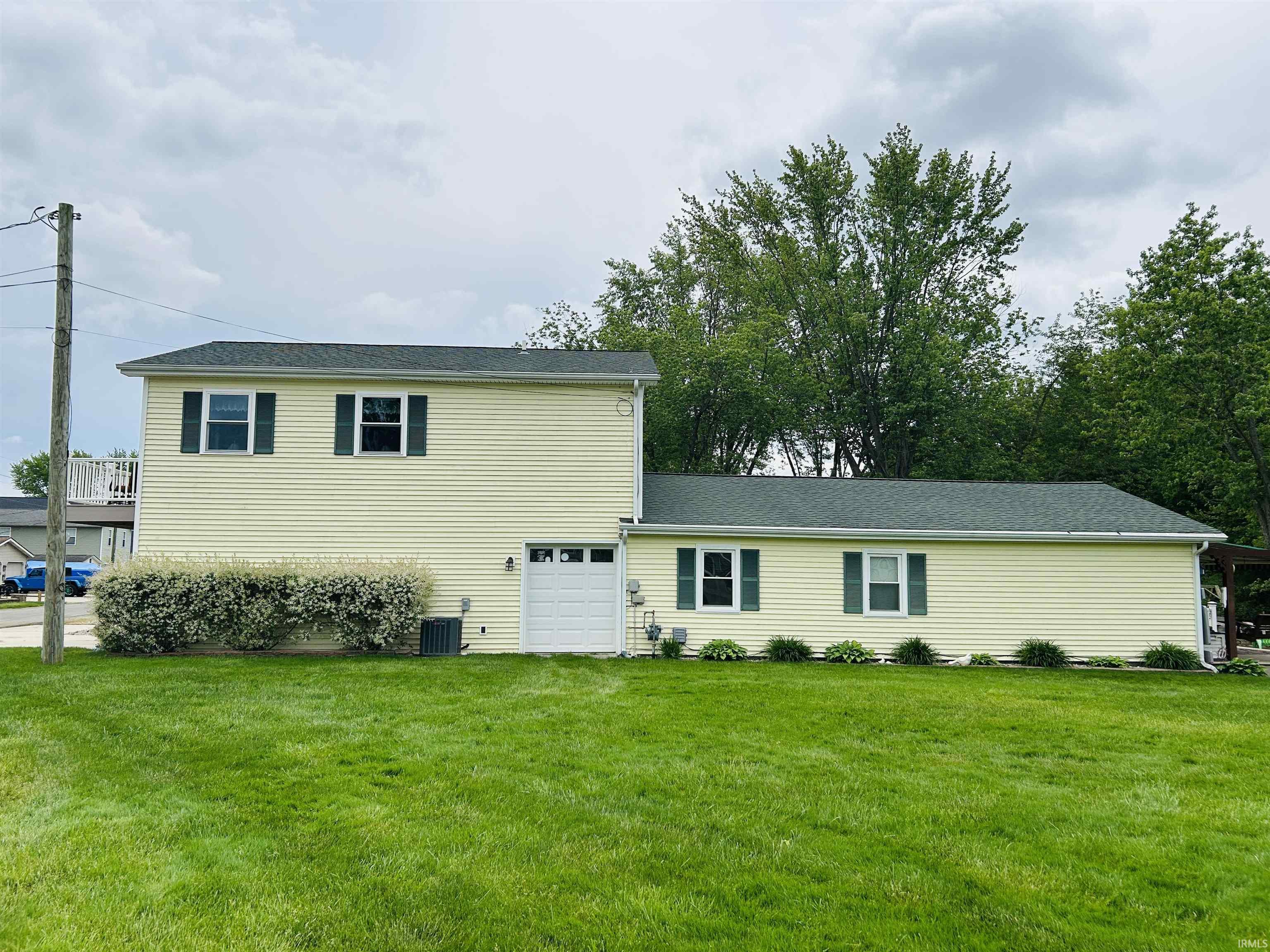 Two-story residence featuring light yellow siding and a dark green roof