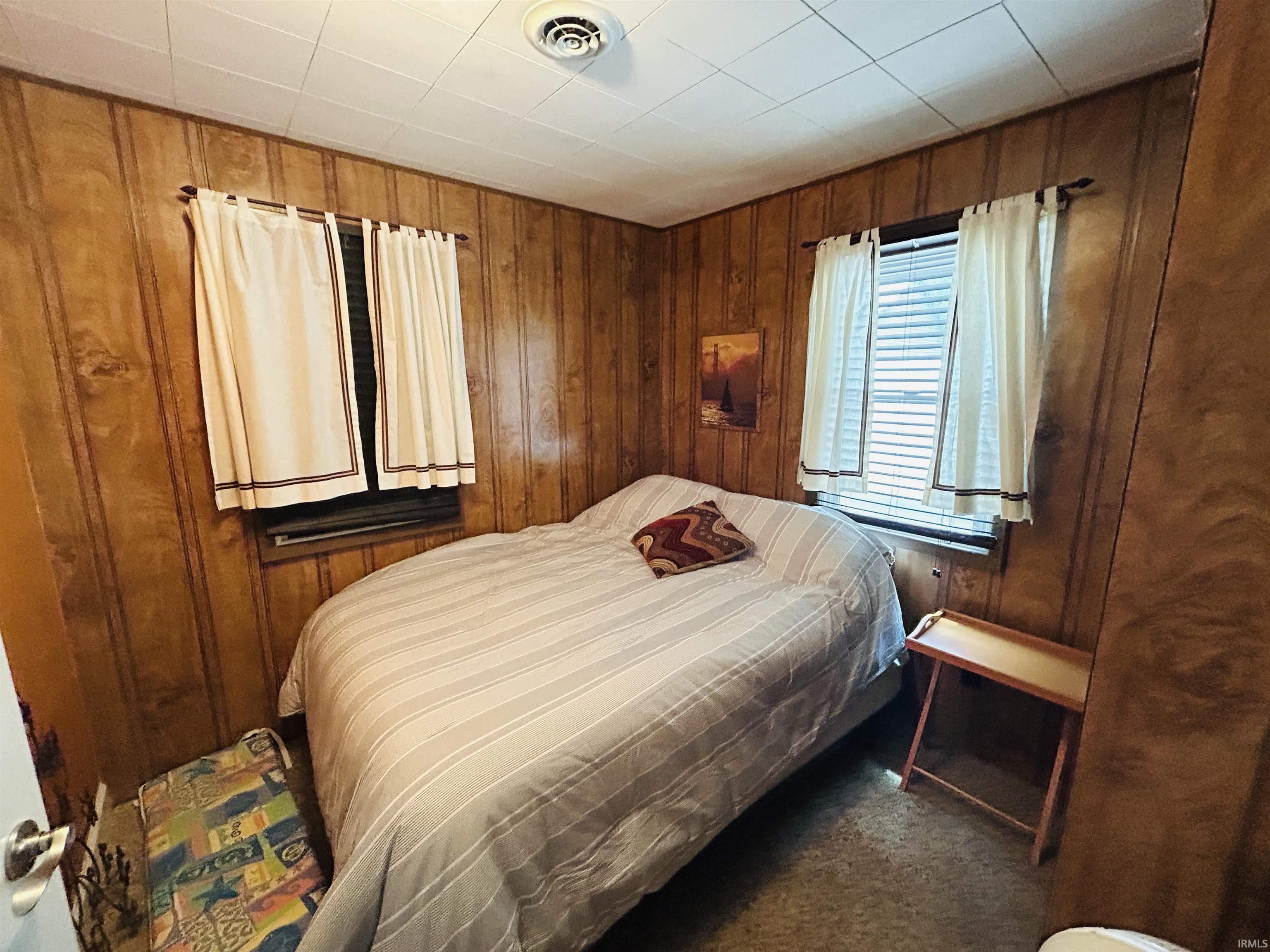 Interior room featuring wood-panel walls, a white acoustic tile ceiling, and carpeting