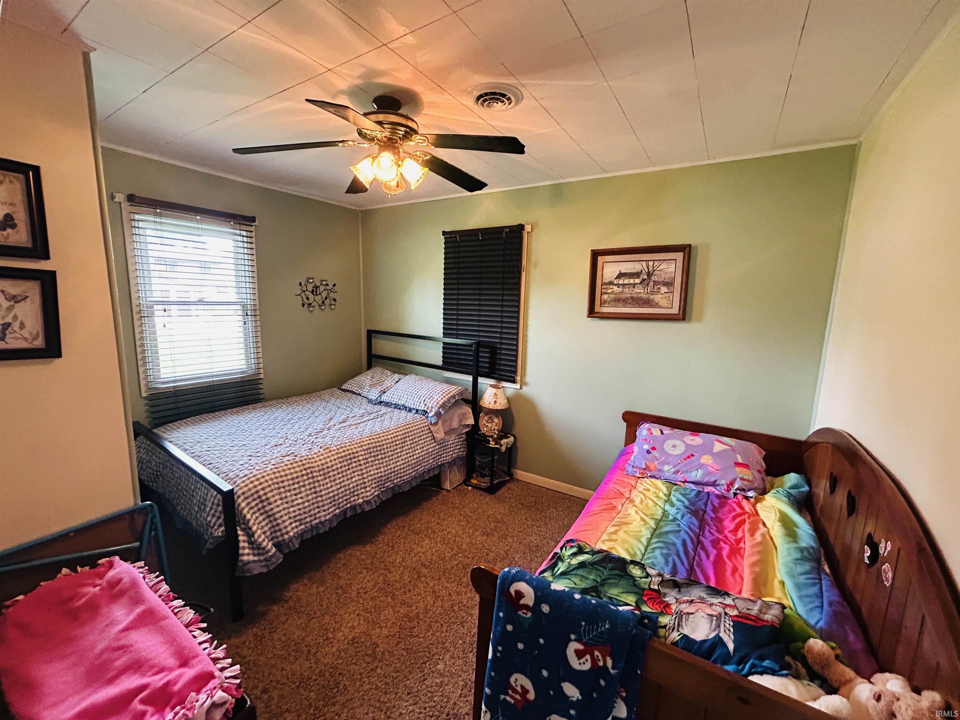 Carpeted room featuring a ceiling fan with integrated lighting, two windows with blinds, and light green wall paint