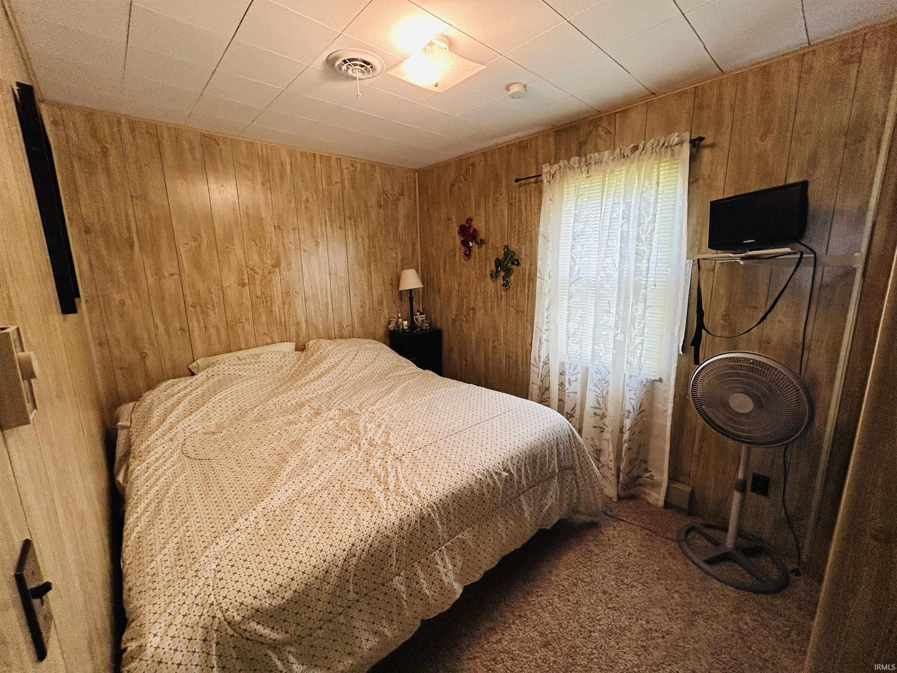 Bedroom featuring wood-finish paneling, carpeted flooring, and a single window with curtain rods