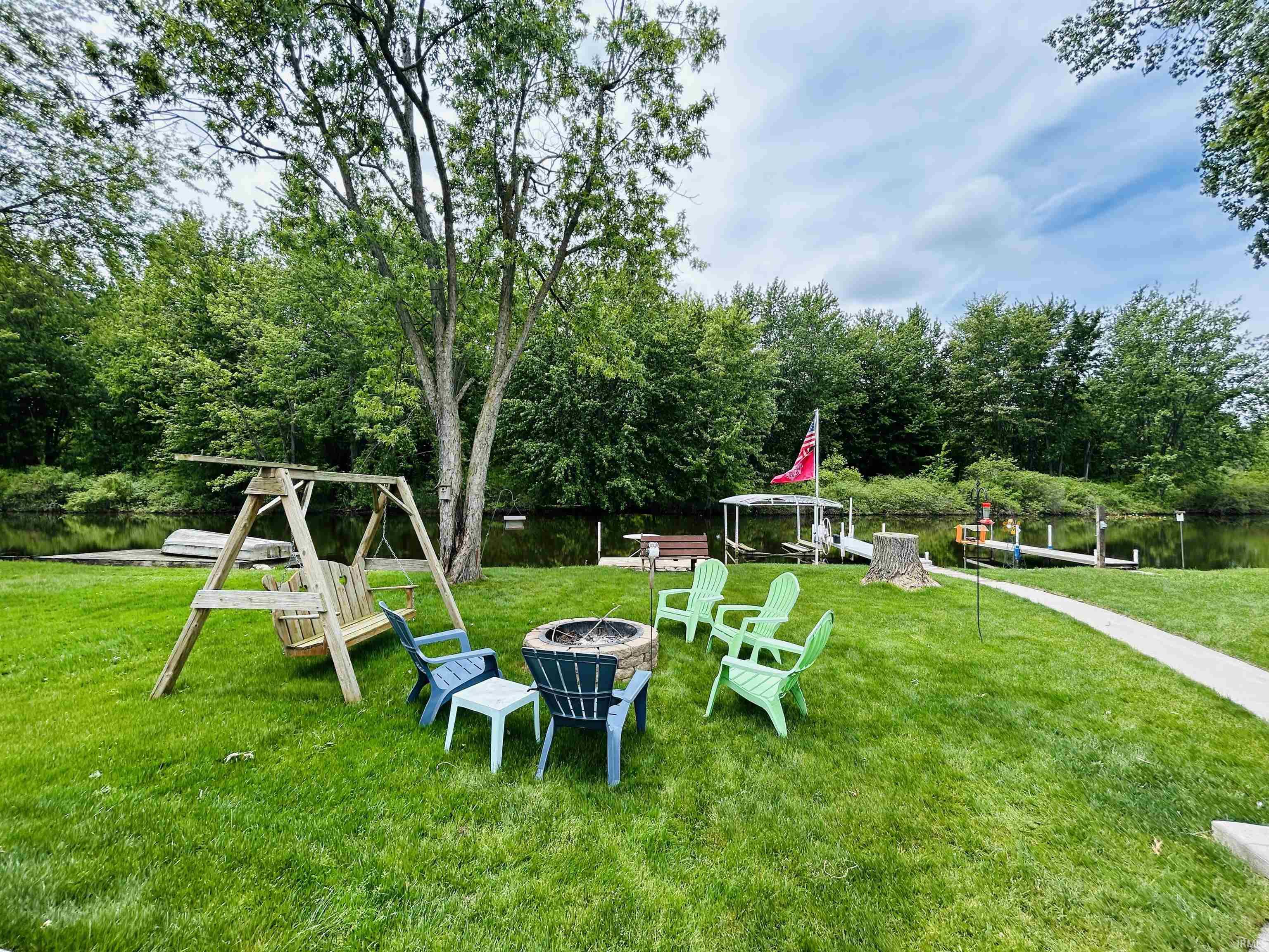Expansive lawn featuring a built-in fire pit, a wooden swing set, and a concrete pathway