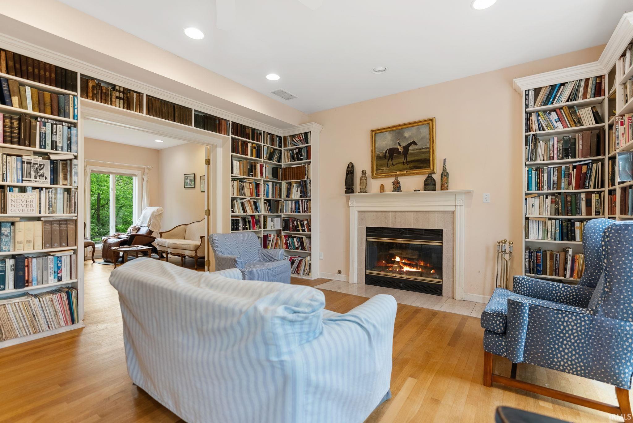 Living area featuring extensive built-in bookshelves, a central fireplace with a decorative mantelpiece, light wood-finish flooring, and recessed ceiling lighting