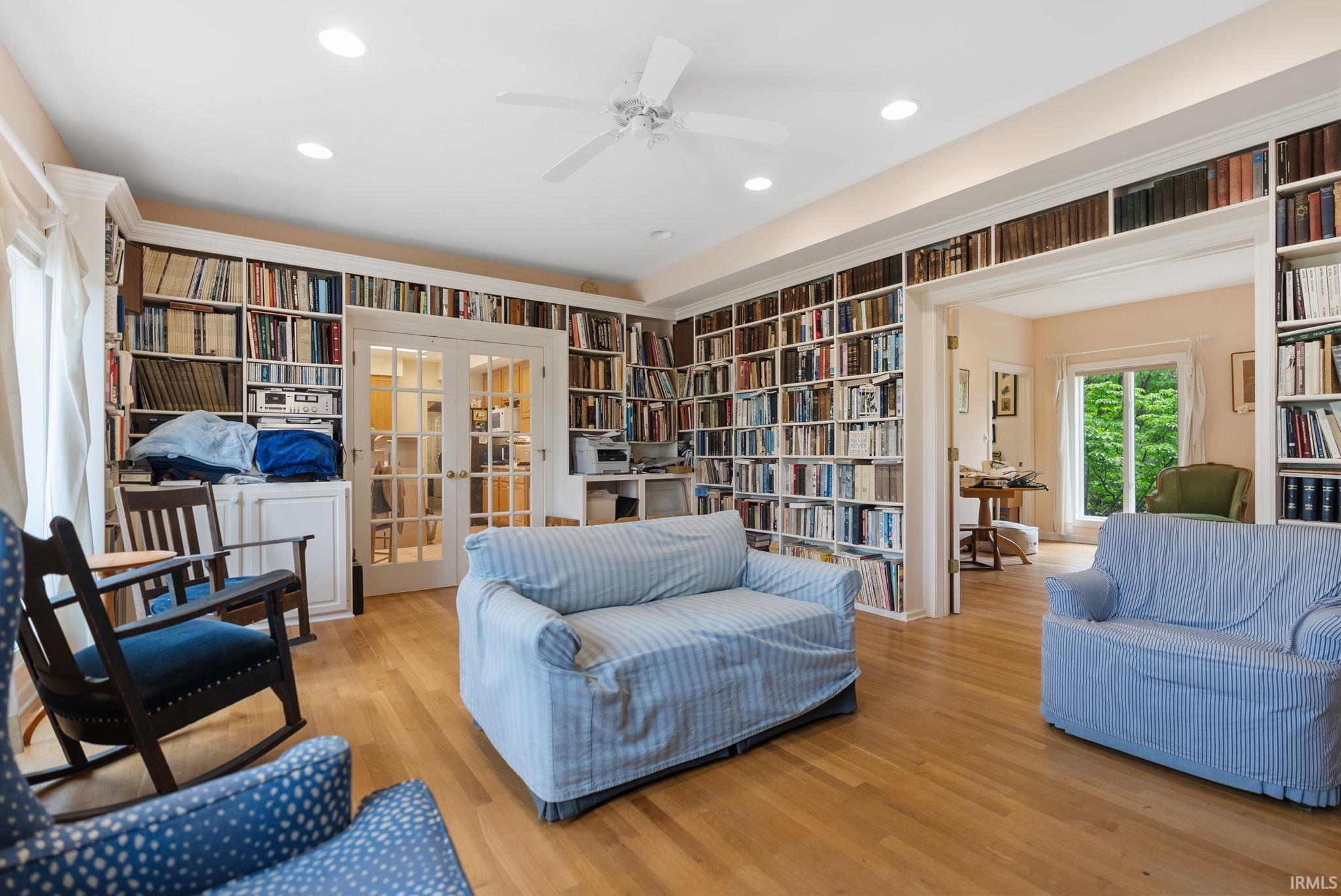 Expansive room featuring floor-to-ceiling built-in bookshelves, light wood-finish flooring, recessed lighting, and a ceiling fan