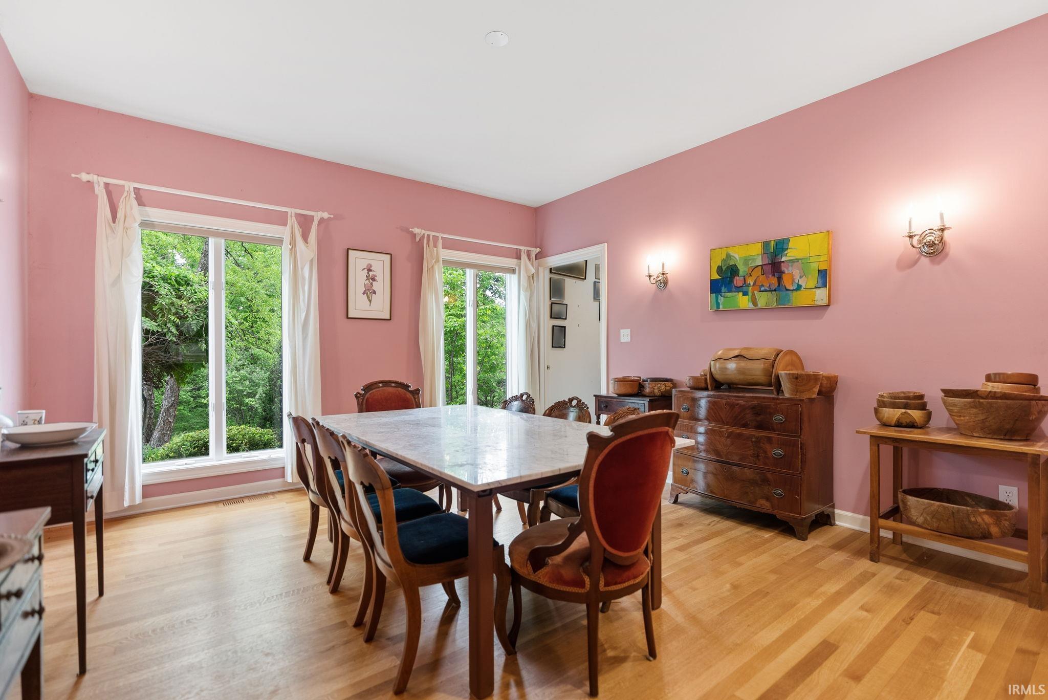 Dining area featuring light wood-finish flooring, two large windows, a glass-paned door, and wall-mounted sconces