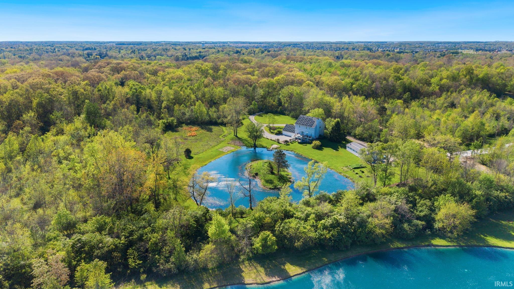 Expansive estate featuring a private pond with a central island, surrounded by abundant mature trees and manicured lawns
