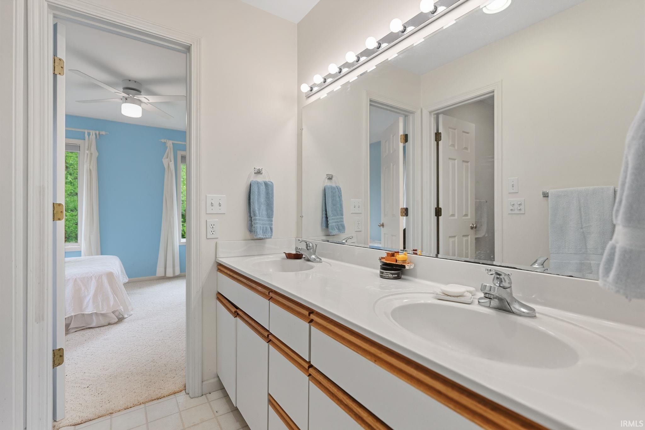 Double vanity with integrated sinks, white cabinetry, wood-finish trim, and a full-width mirror