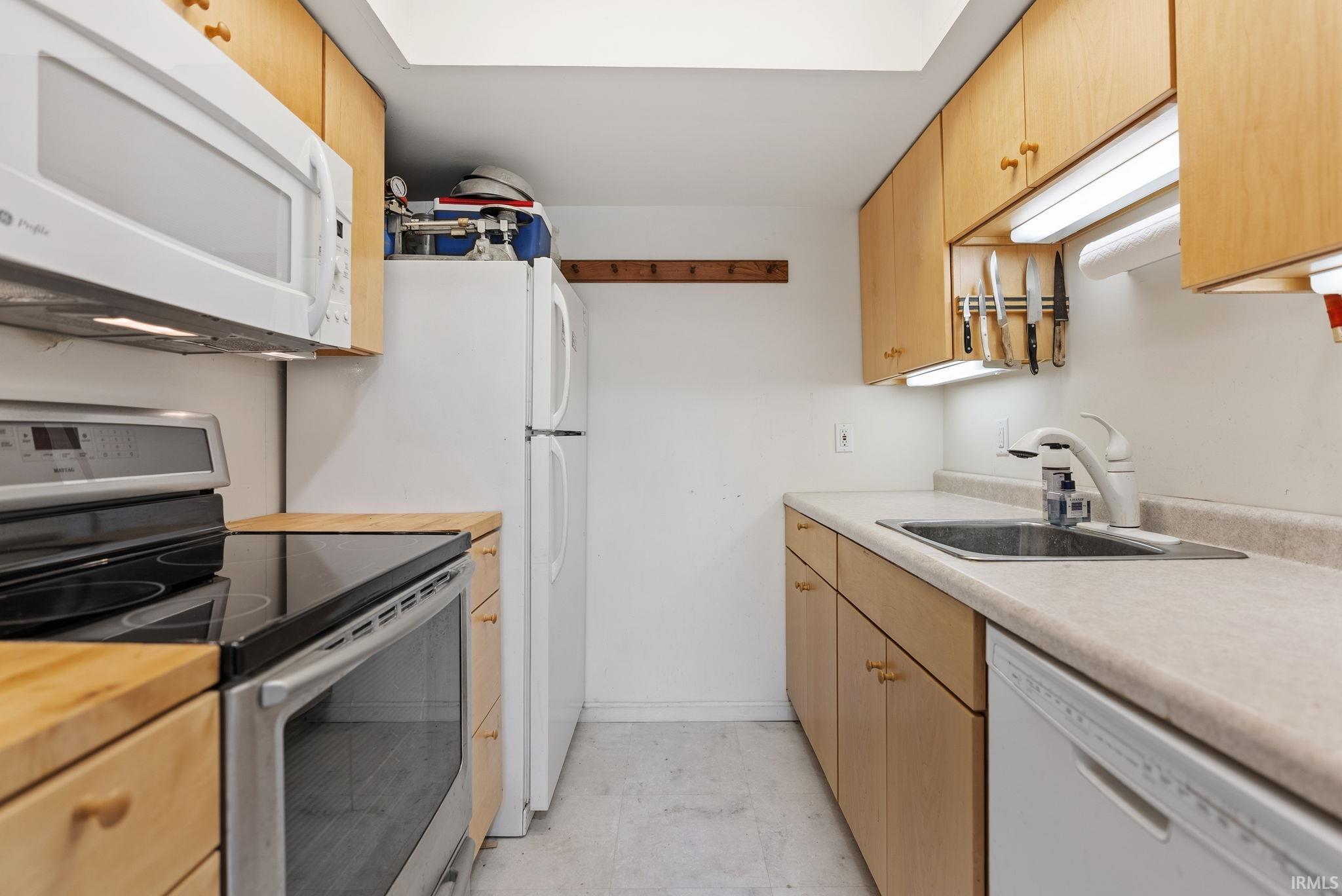Efficient kitchen featuring light wood cabinetry, white appliances, and a stainless steel sink