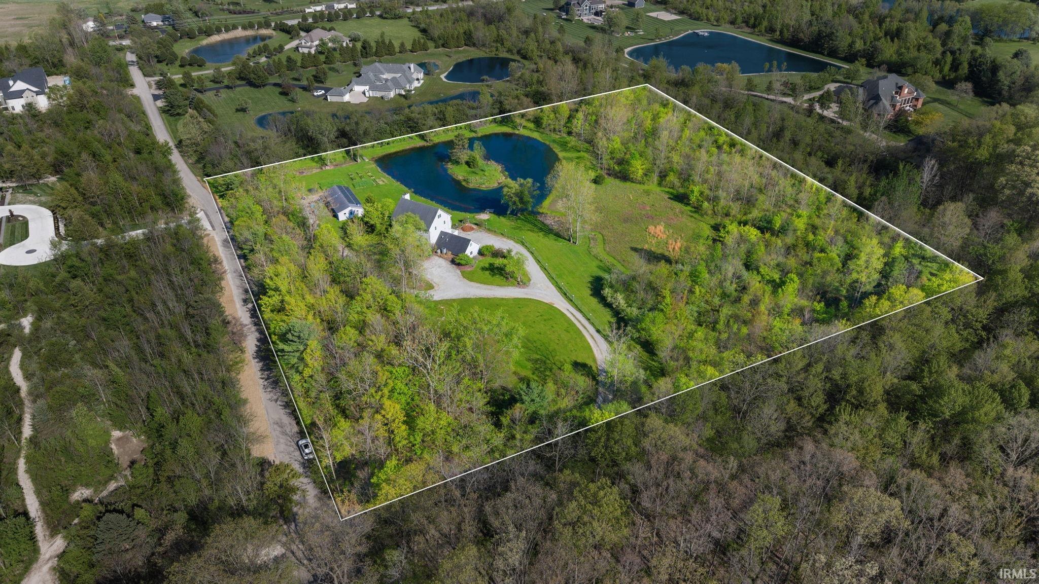 Expansive property featuring a private pond with a central island, a white main residence, and a separate structure