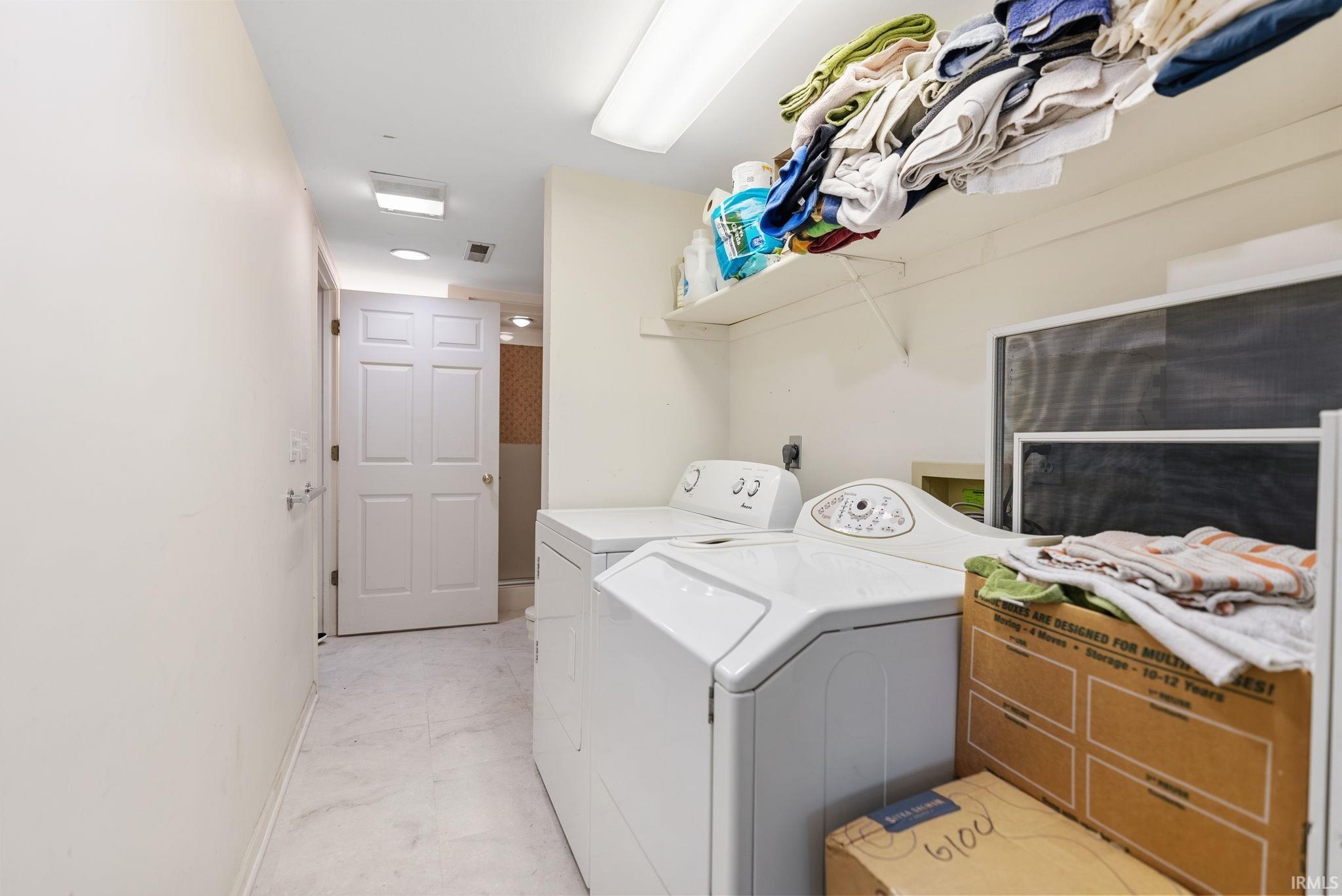 Dedicated laundry area featuring white tile flooring and overhead shelving