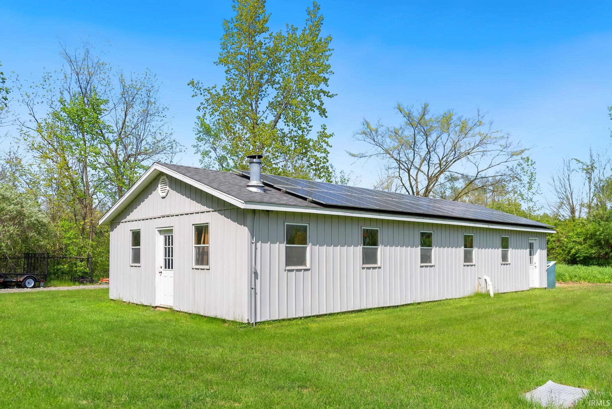 Single-story structure with light grey vertical siding and multiple solar panels across the roofline