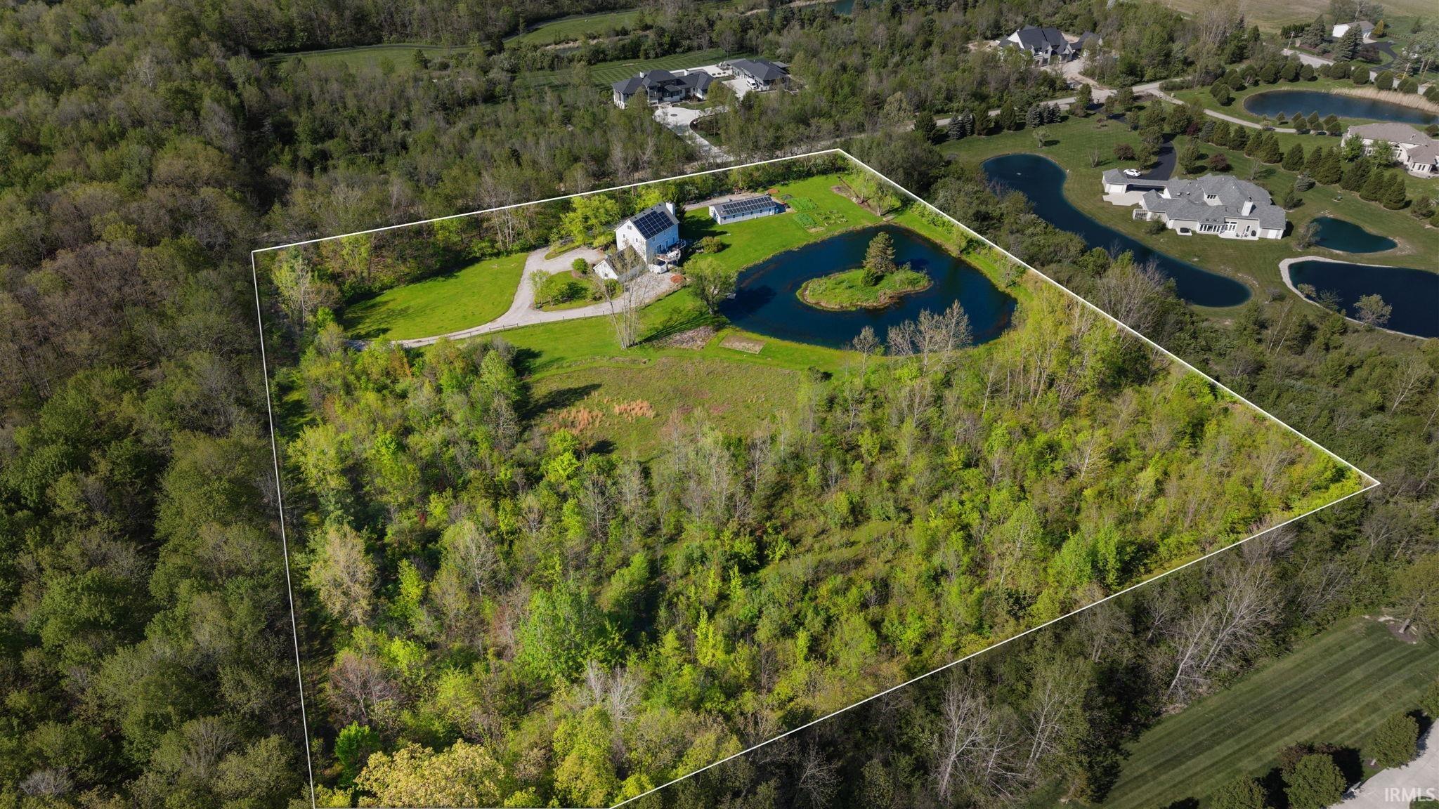 Expansive property featuring a private pond with a central island, a residential structure, a swimming pool, and extensive wooded areas