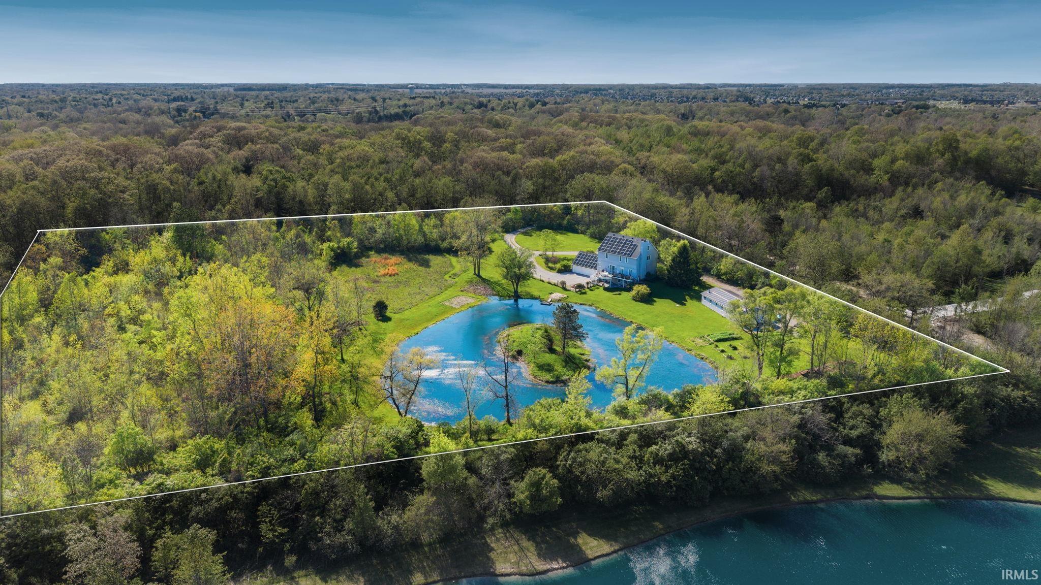 Expansive property featuring a private pond with a central island, surrounded by abundant mature trees and lush green landscaping