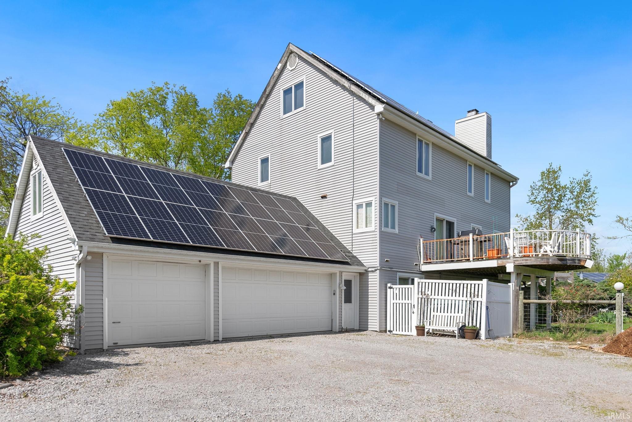 Two-car garage with installed solar panels, light gray siding, and a white deck with railings