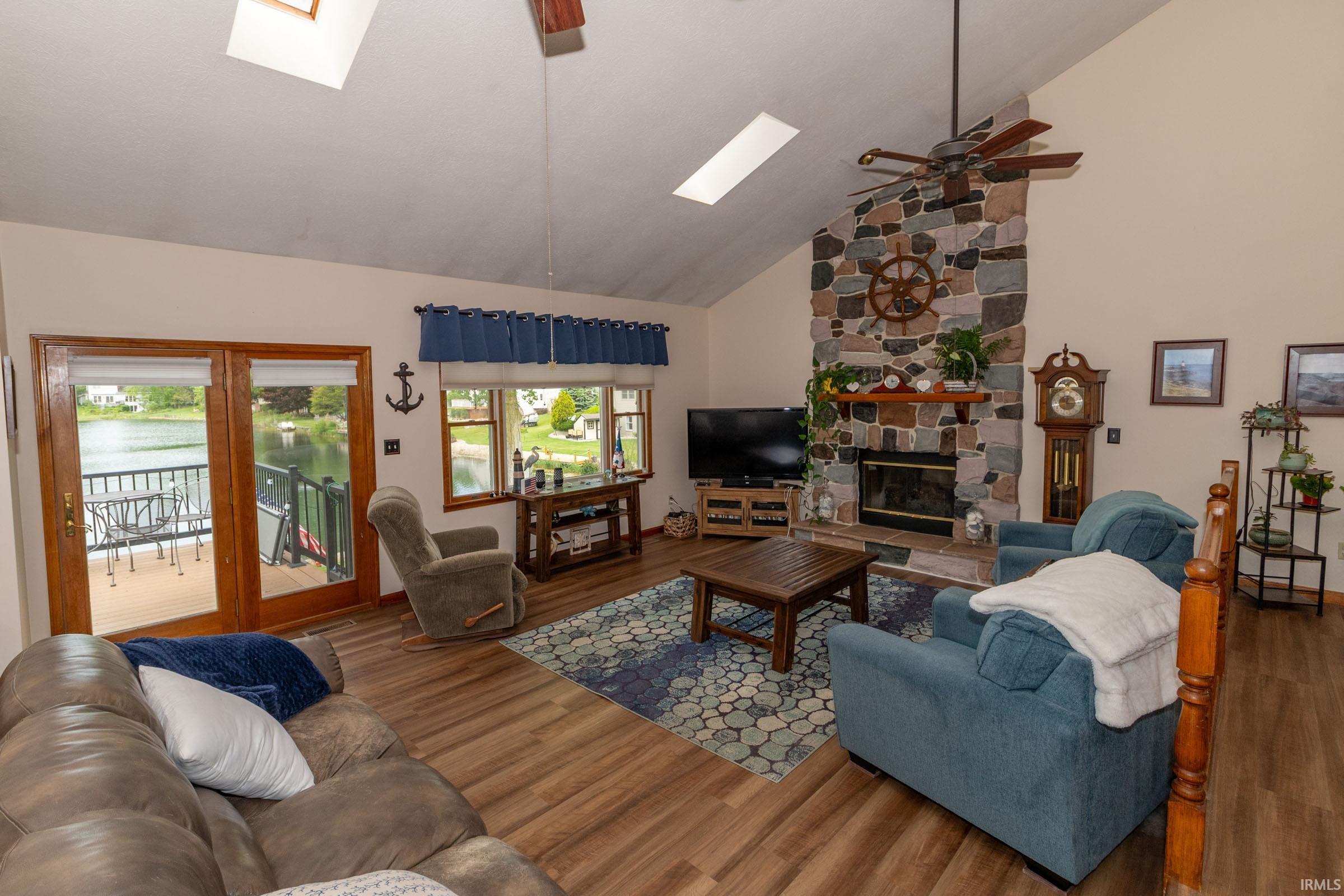 Spacious living area featuring a stone-clad fireplace, vaulted ceiling, wood-finish flooring, and skylights