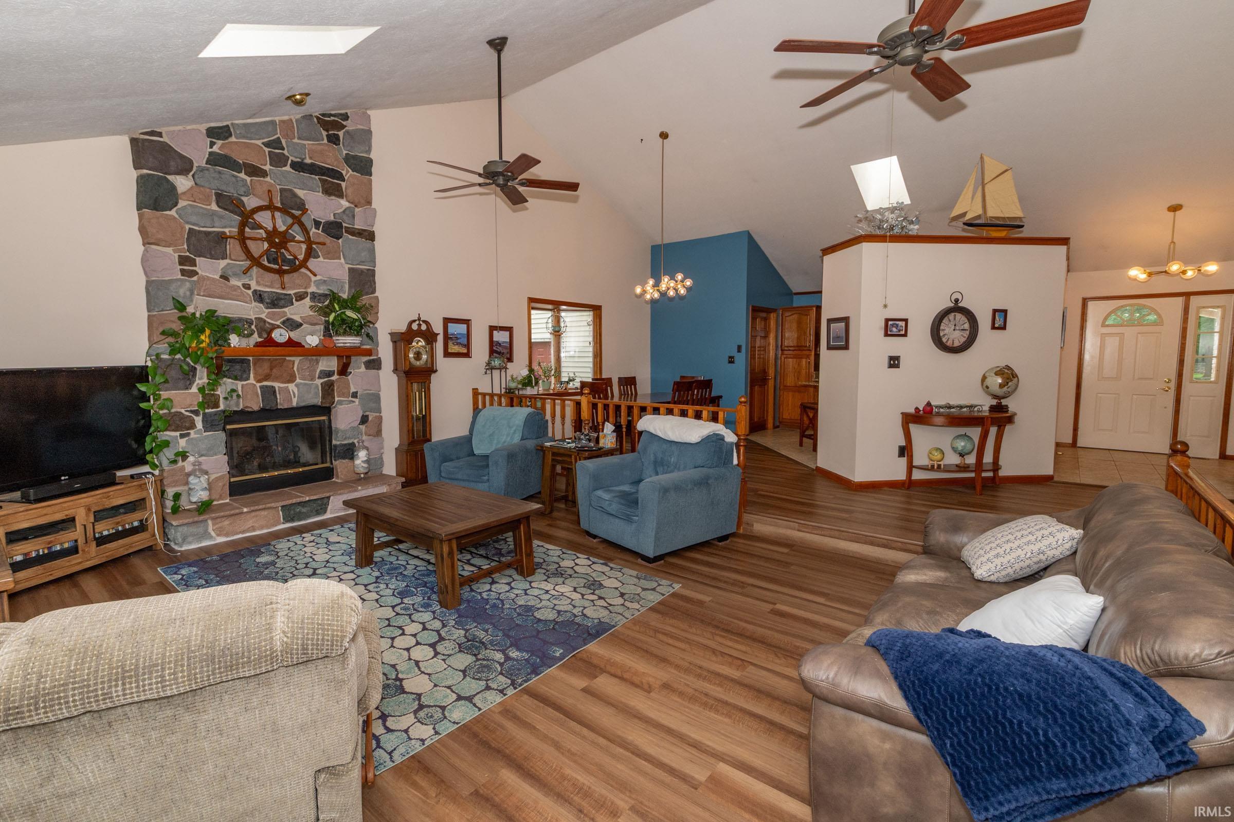 Living area featuring a stone fireplace with a wood mantle, vaulted ceilings with skylights, and wood-finish flooring