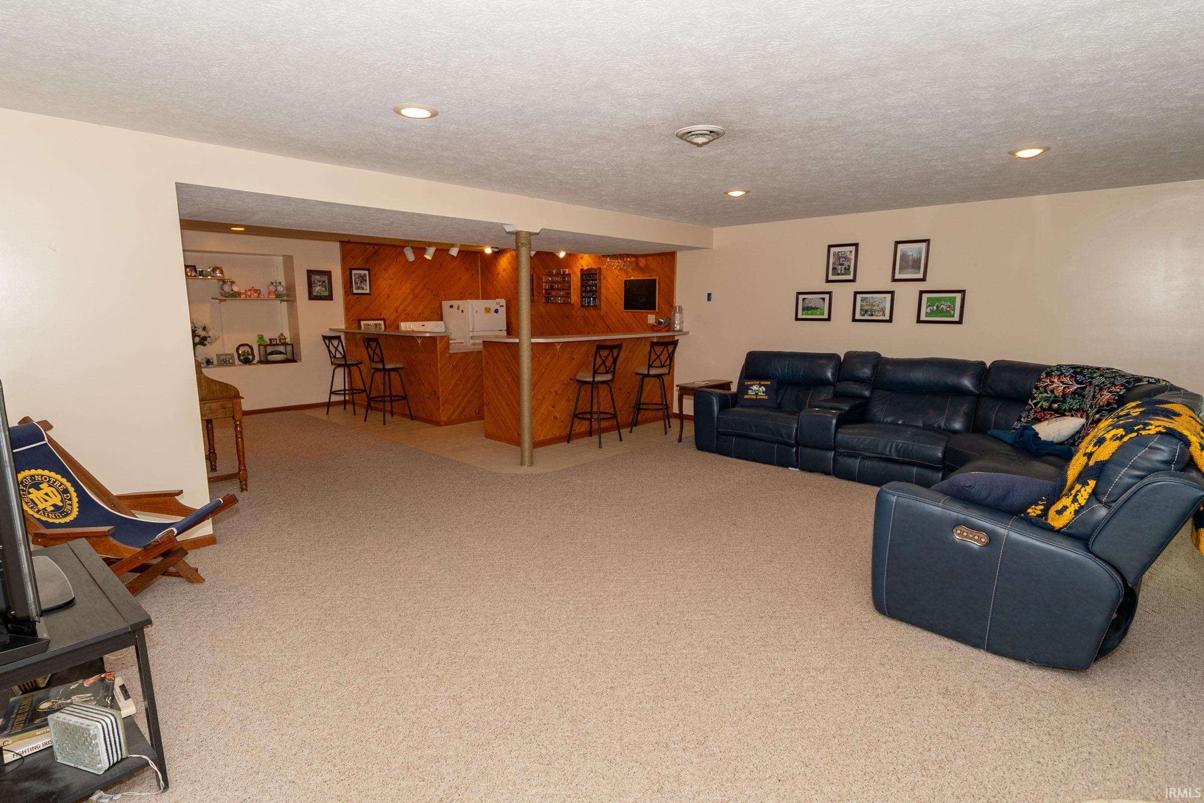 Spacious finished lower level with recessed lighting, carpeted flooring, and a built-in wet bar featuring wood paneling, track lighting, and a white refrigerator