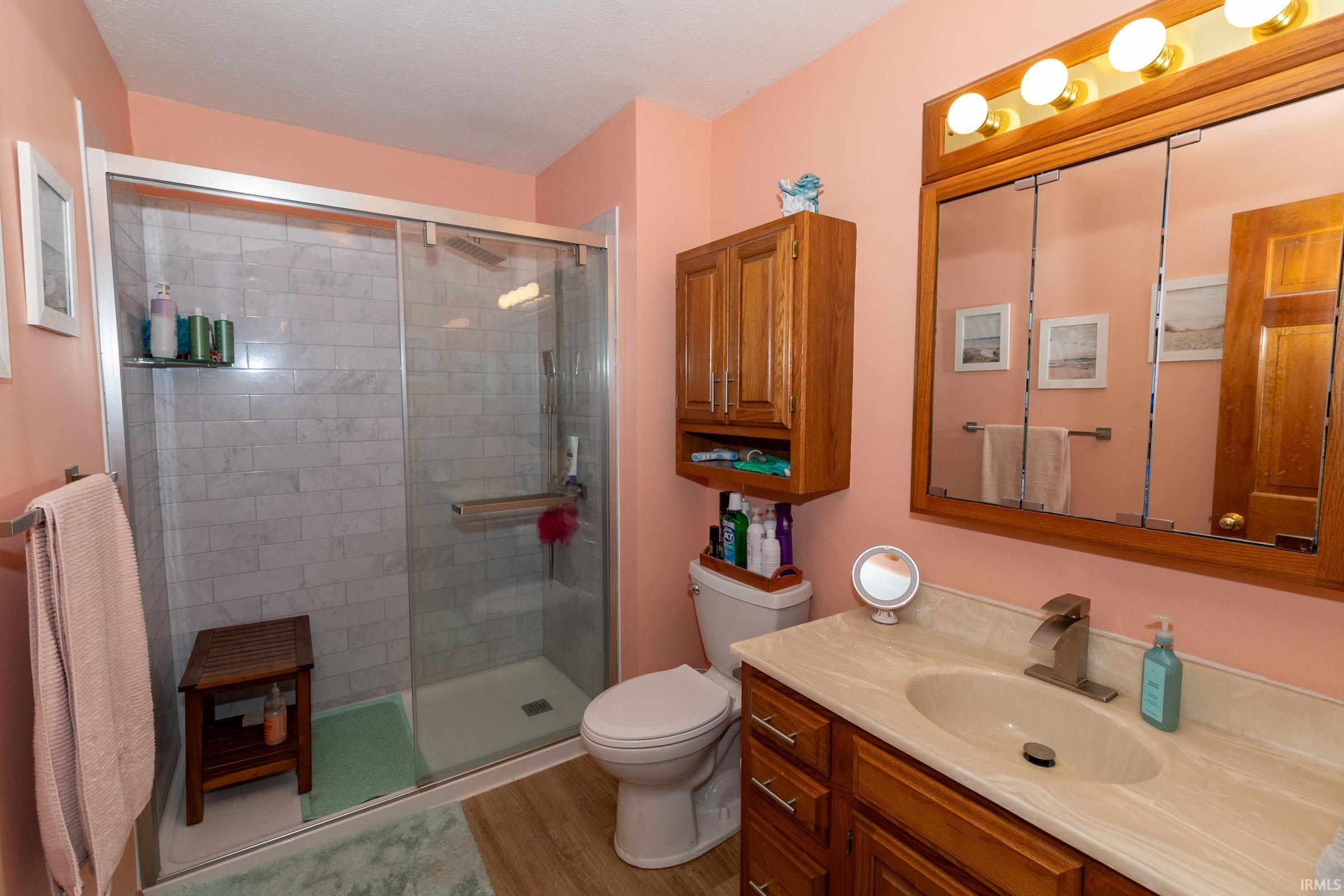 Bathroom featuring a glass-enclosed shower with subway tile surround, single vanity with a light-toned countertop, and recessed medicine cabinet with integrated lighting