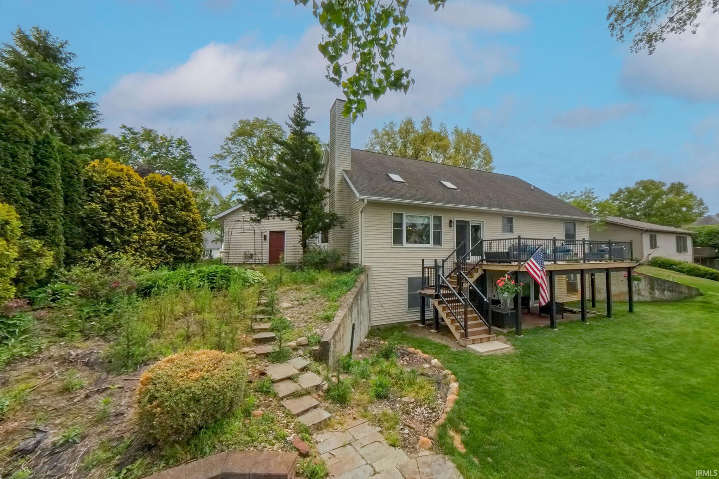 Split-level exterior featuring a multi-tier wood deck, black metal railings, and a lower-level patio
