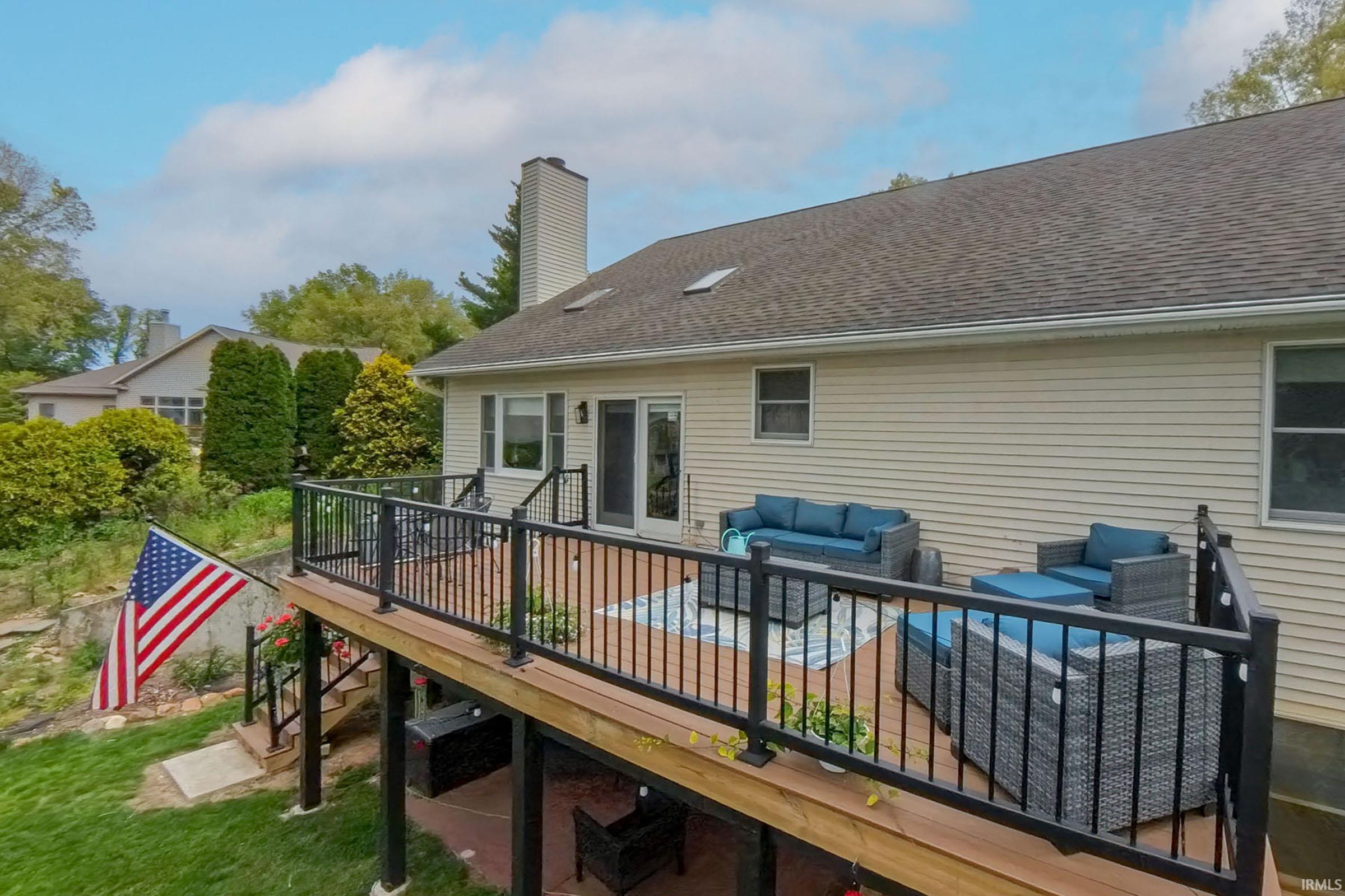 Multi-level exterior deck featuring wood-finish decking, black aluminum railings, and stairs descending to a lower patio