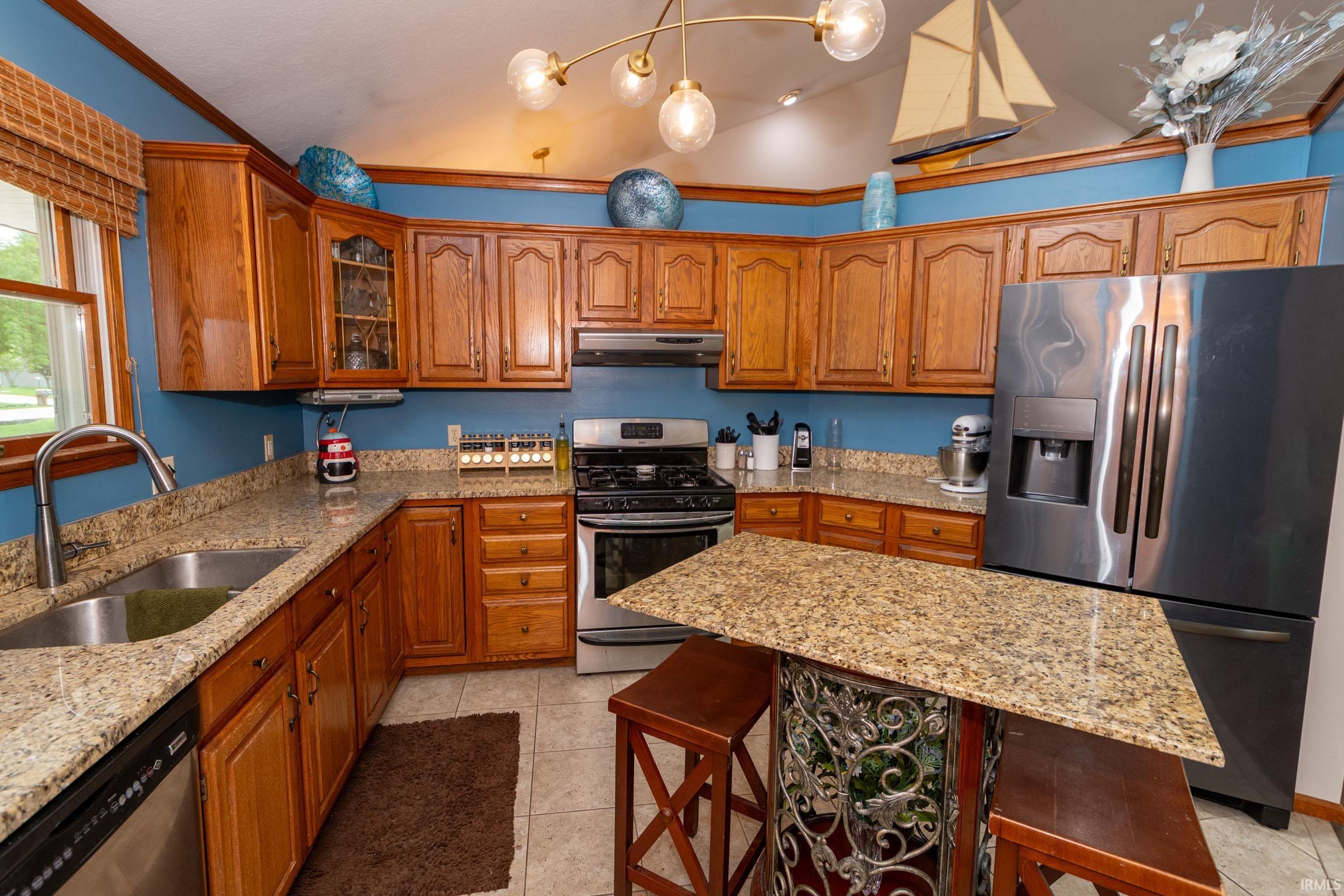 Kitchen featuring wood cabinetry, granite countertops, stainless steel appliances, a built-in double sink, and a breakfast bar