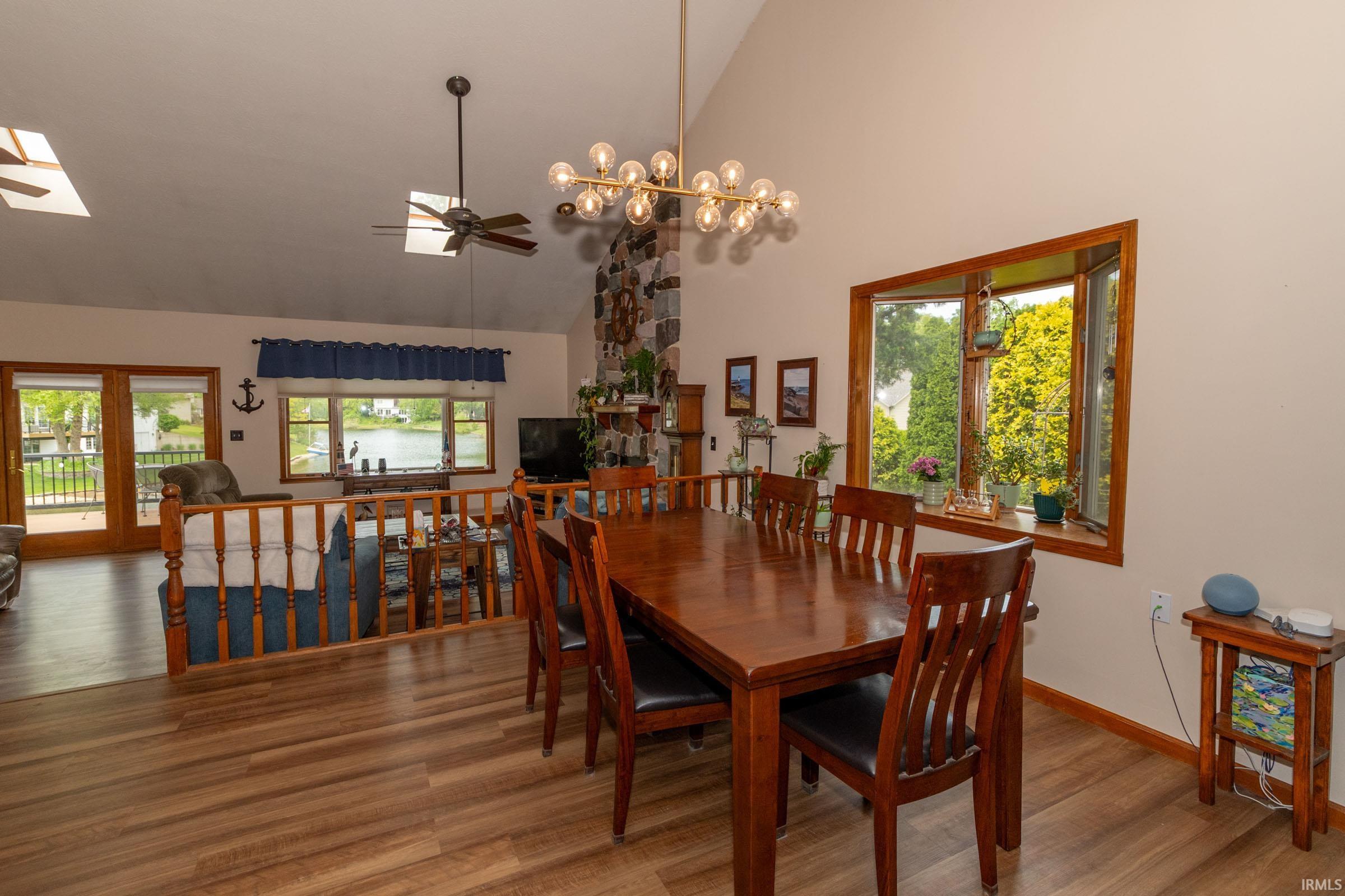 Vaulted ceiling dining area featuring wood-finish flooring, a contemporary chandelier, a large bay window, and a half-wall overlooking a sunken living area