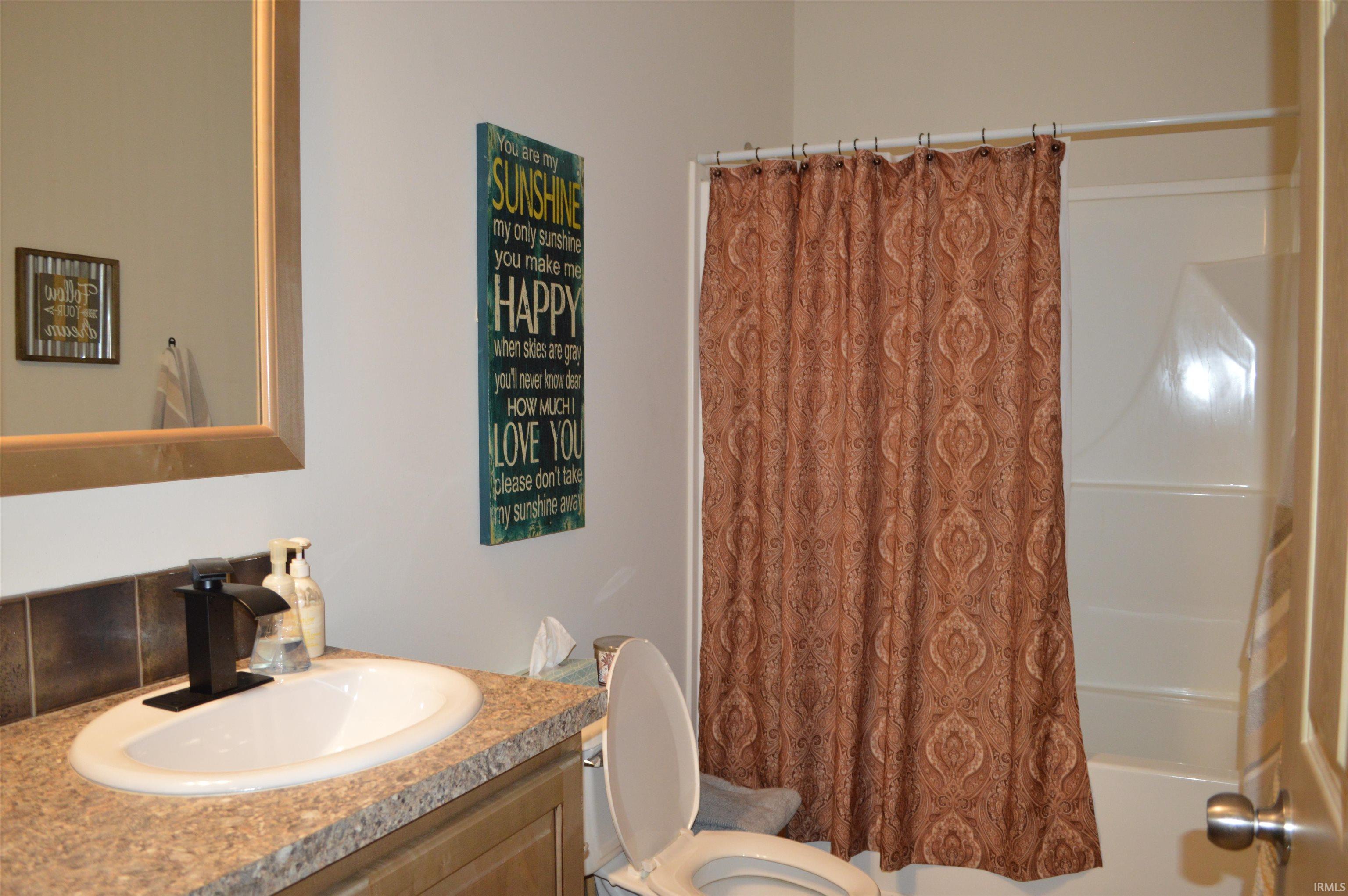 Bathroom featuring a shower/tub combination with a white surround, a vanity with a countertop, an undermount sink, and a black faucet, and a wall-mounted mirror with a wooden frame