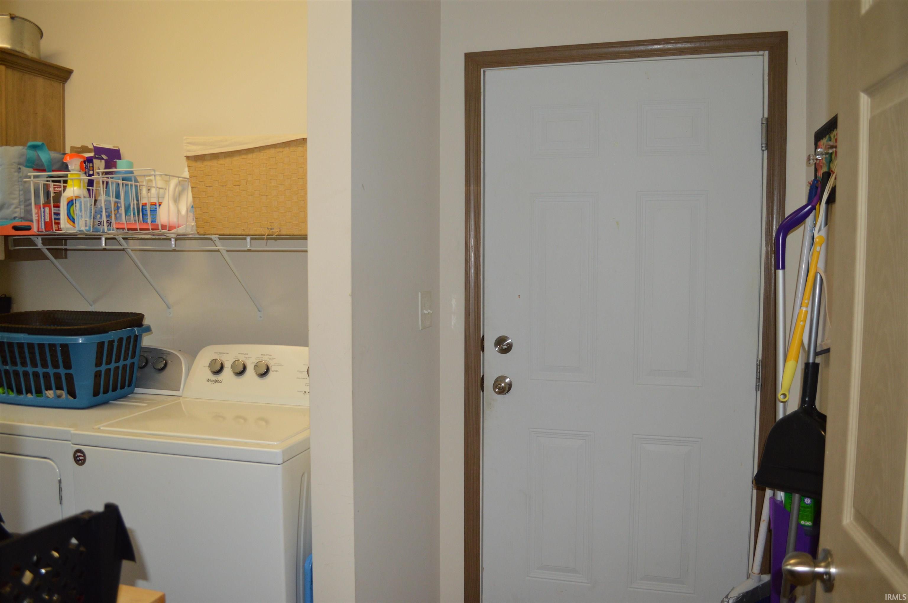 Utility area featuring a white paneled door with wood-finish trim, a wire shelving unit, and a built-in wood-finish cabinet