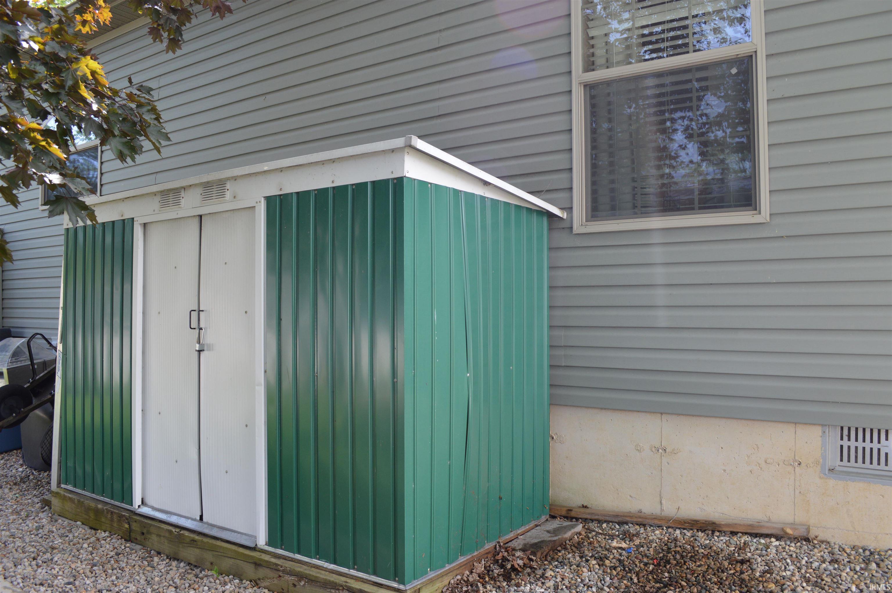 Compact outdoor storage shed featuring dual white doors and green corrugated metal siding