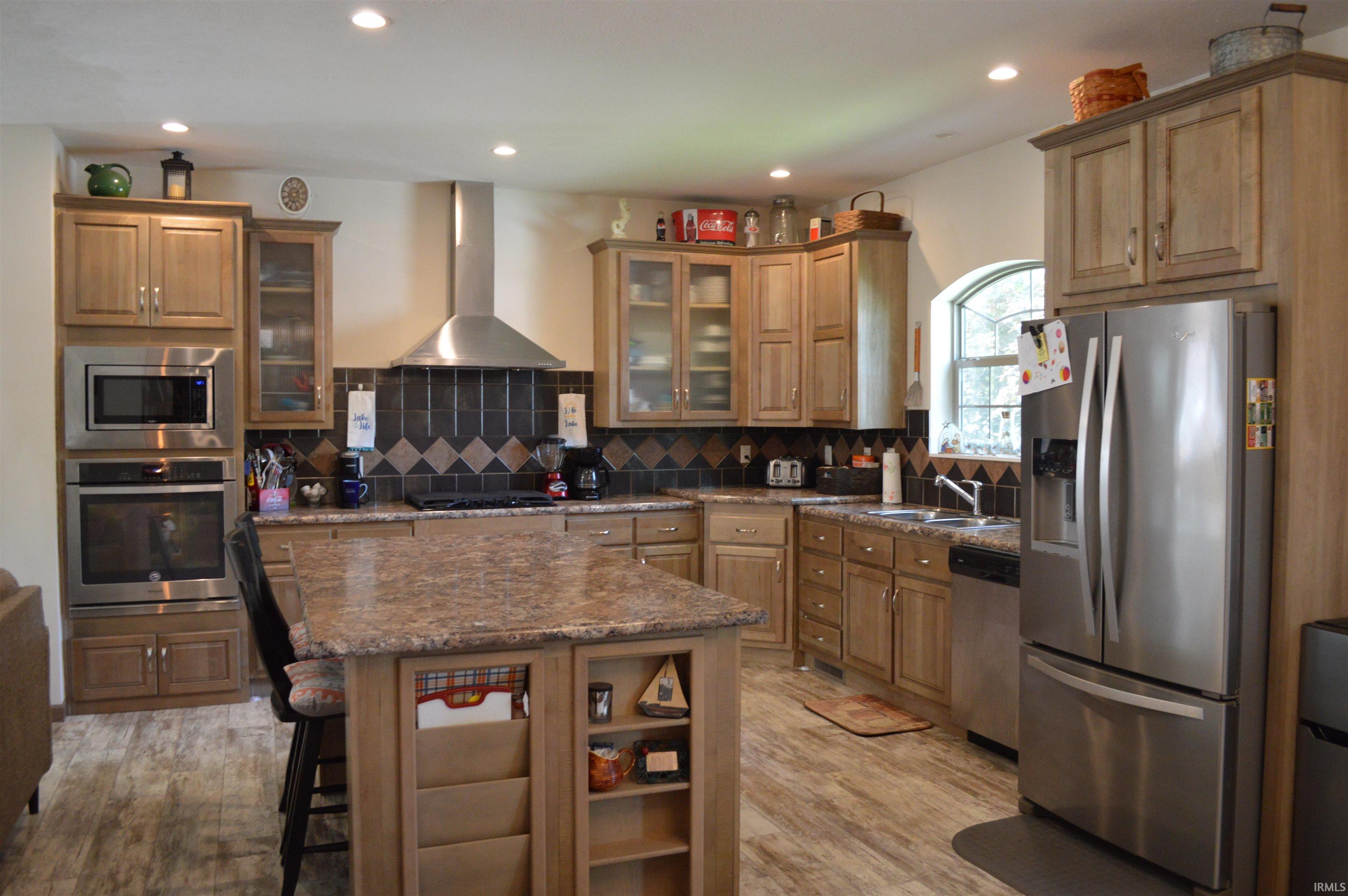 Spacious kitchen featuring wood-finish cabinetry, stainless steel appliances, a center island with granite-style countertop, a tile backsplash, and recessed lighting