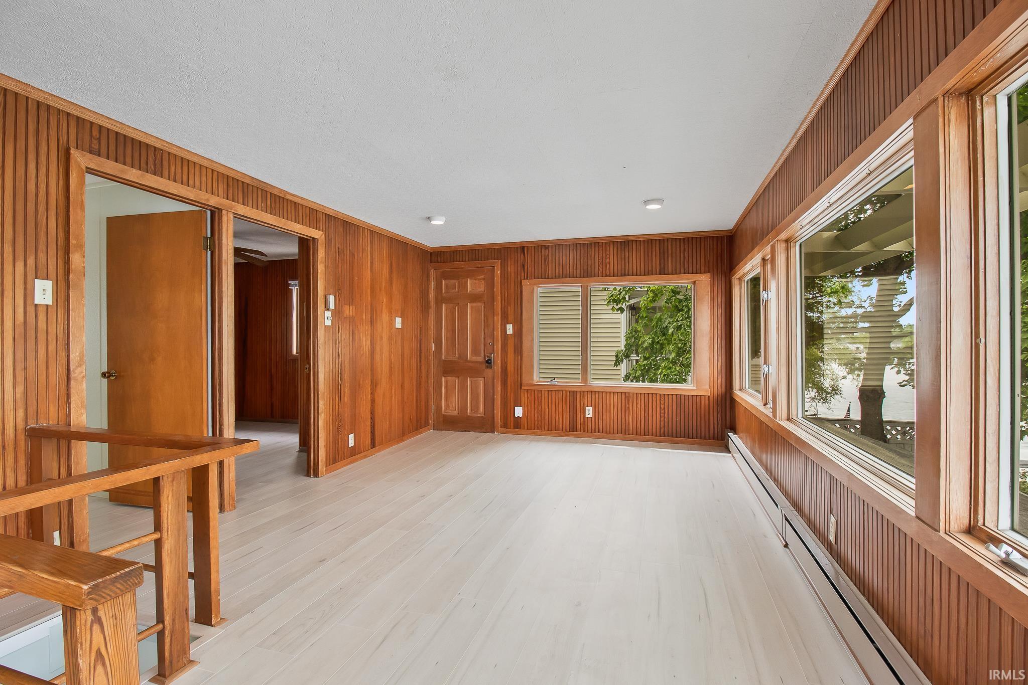 Room featuring extensive wood paneling, light wood-finish flooring, multiple windows, recessed lighting, and a wood railing