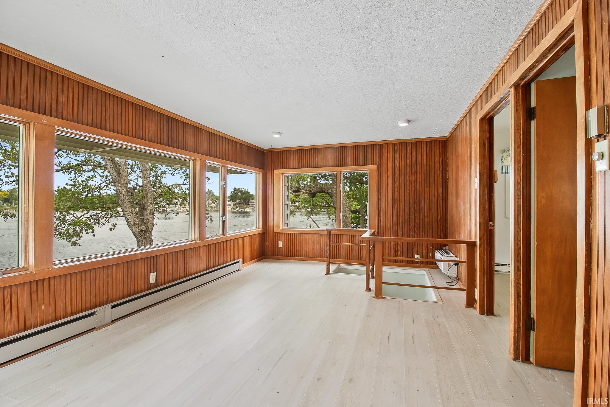 Bright interior space featuring a wall of windows, wood-finish flooring, and natural wood paneling