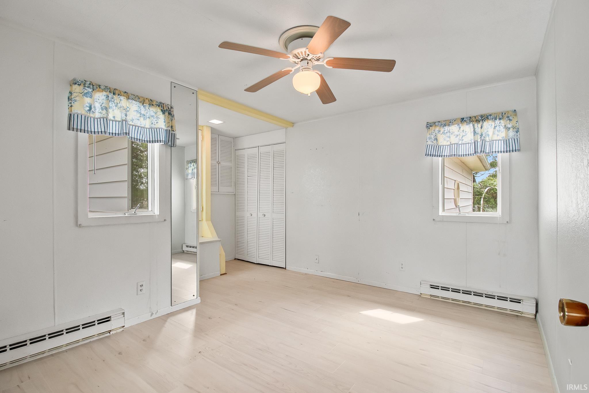 Light wood-finish flooring complements the white walls of this room, featuring two windows with valances