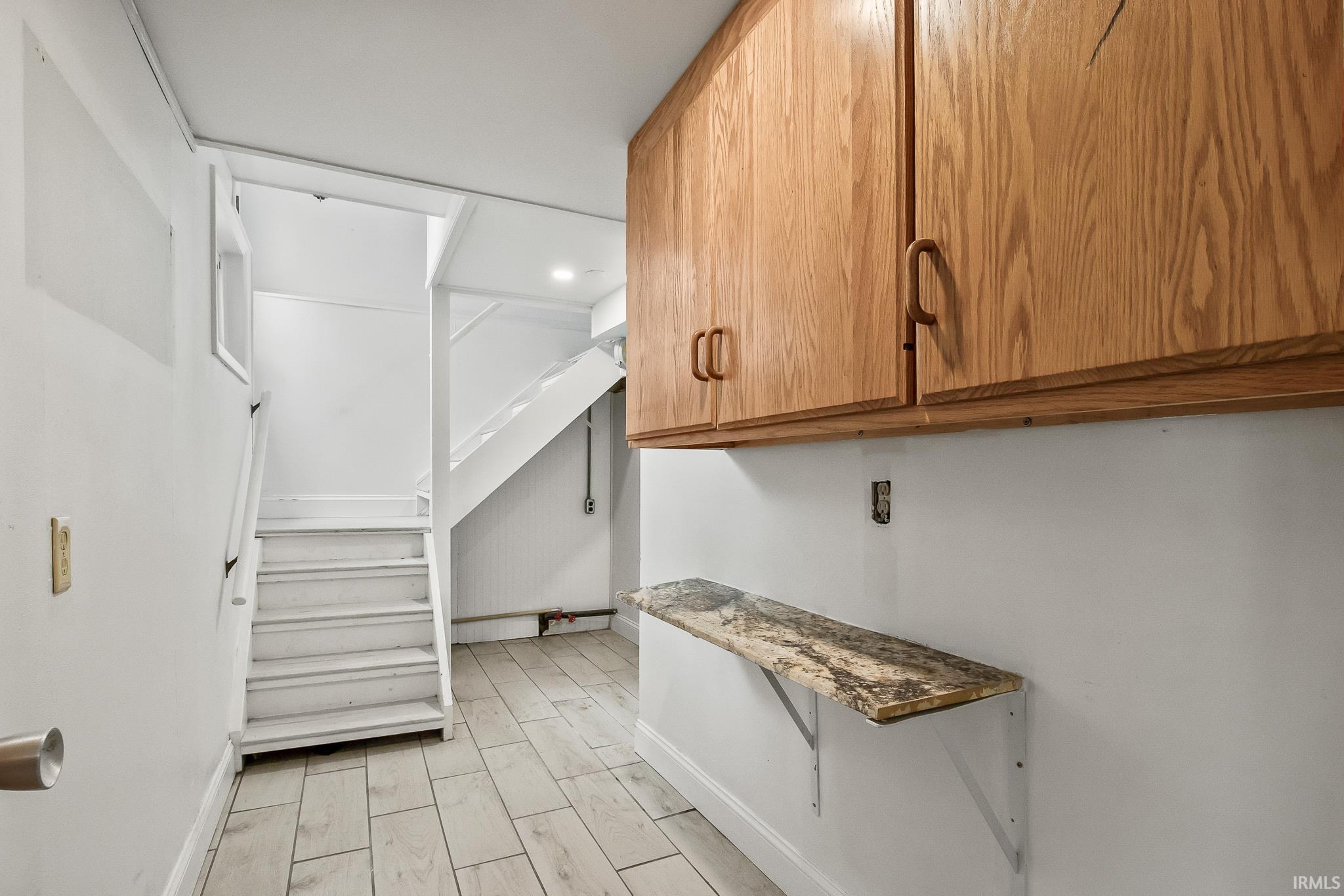 Utility space featuring wood-finish cabinetry, a stone-finish floating shelf, and light-toned tile flooring