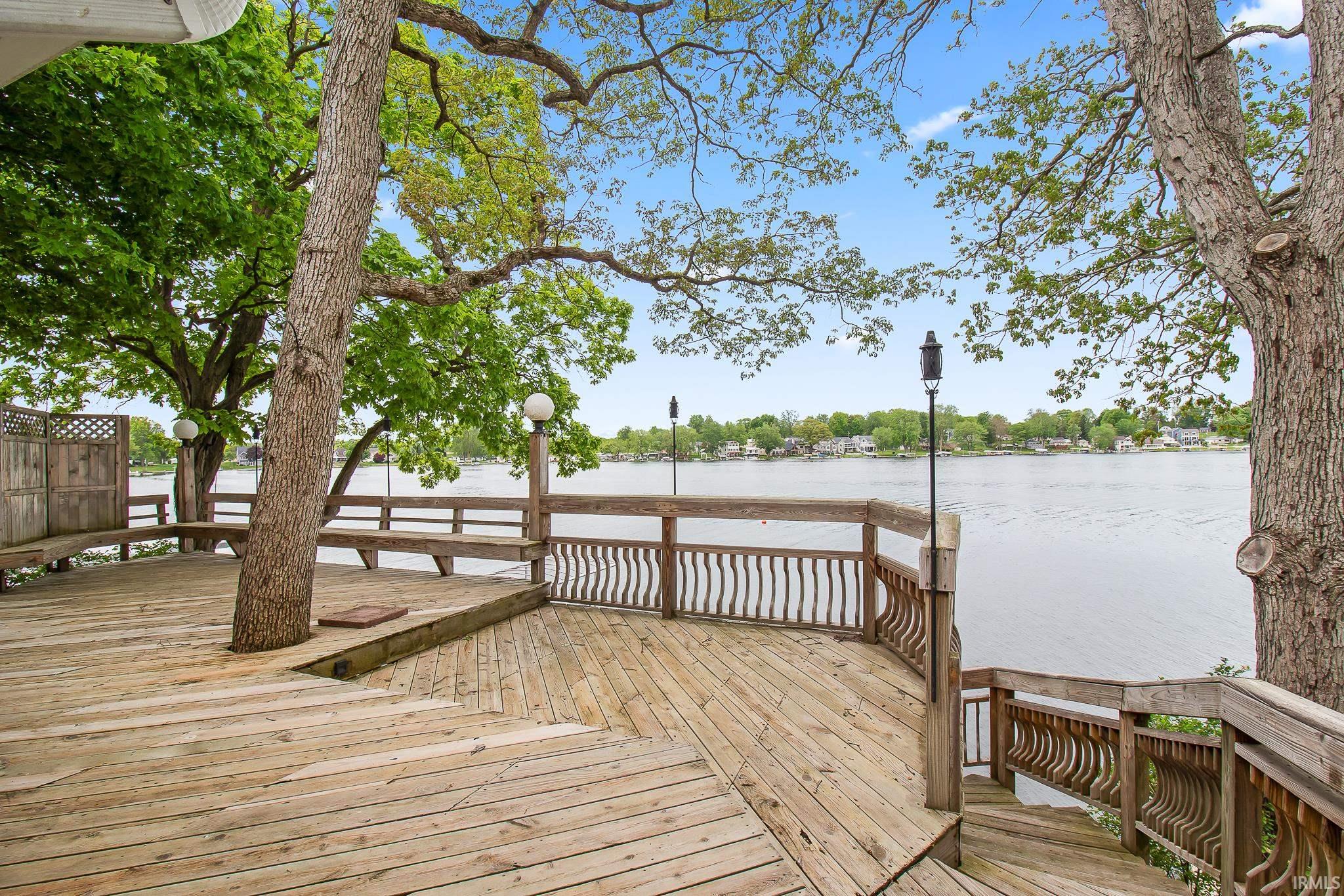 Multi-level wood deck with integrated bench seating, natural tree elements, and a staircase descending to the waterfront