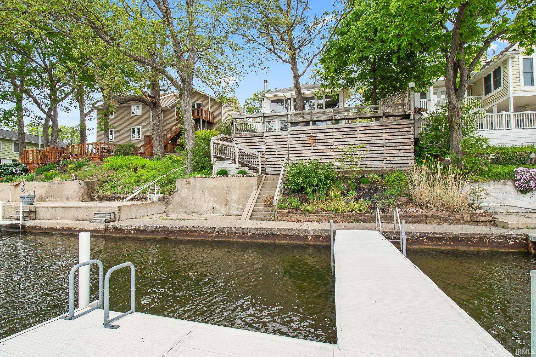 Waterfront property featuring a private dock, concrete retaining wall, and established landscaping