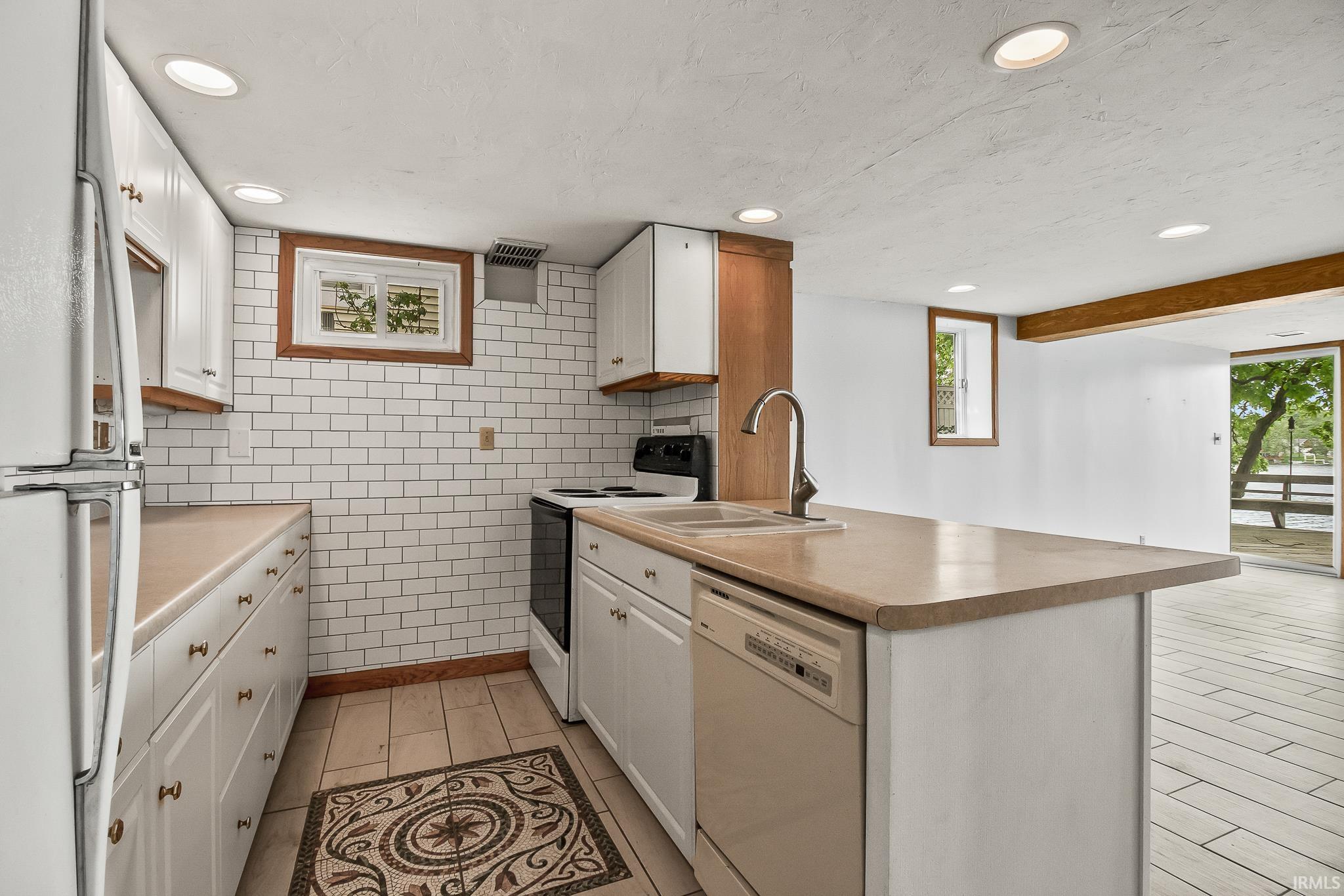 Kitchen featuring white cabinetry, subway tile backsplash, recessed lighting, and a breakfast bar with an integrated sink and dishwasher
