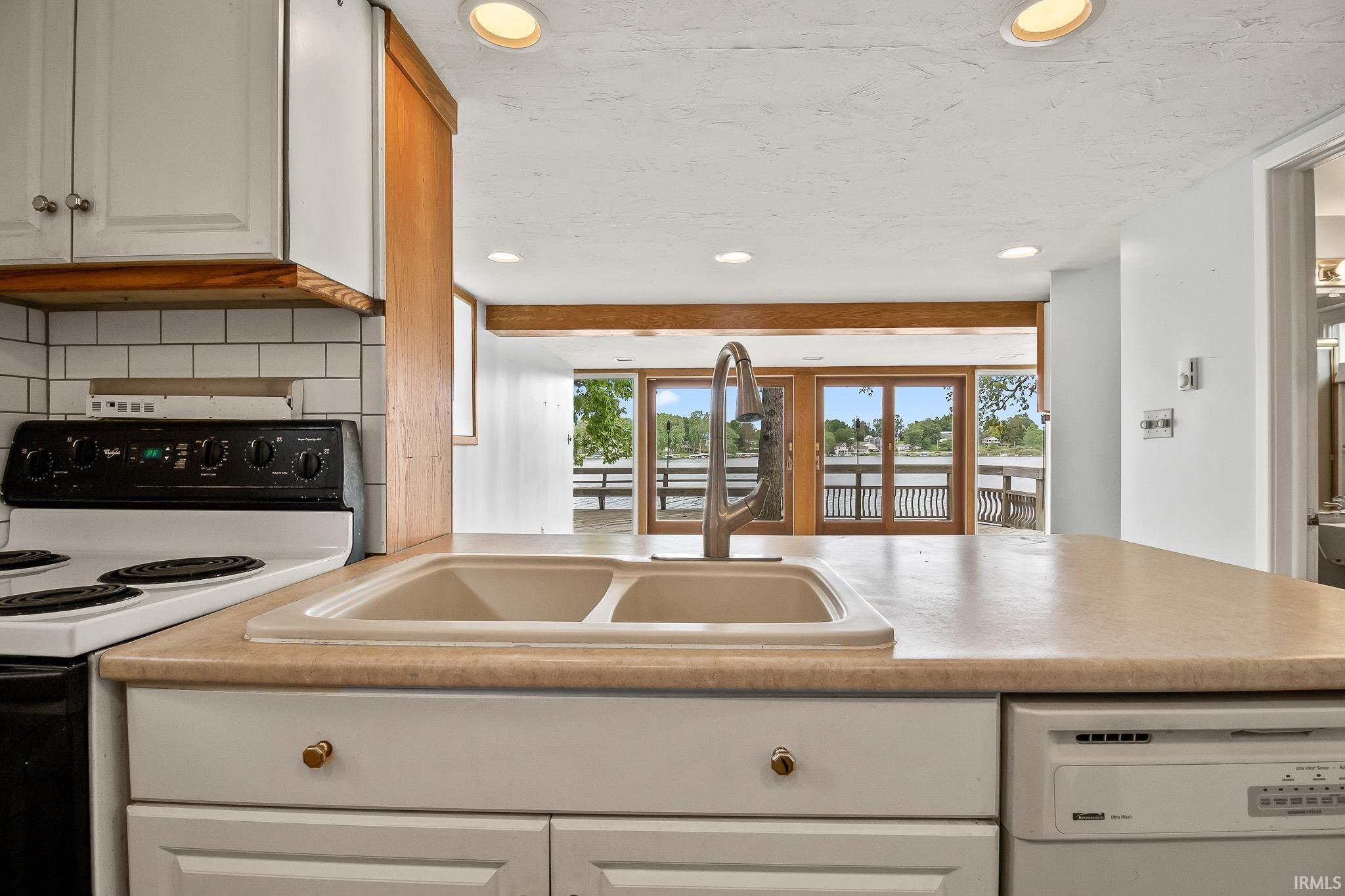 Kitchen featuring a double basin sink with a gooseneck faucet, light-toned countertops, and white cabinetry