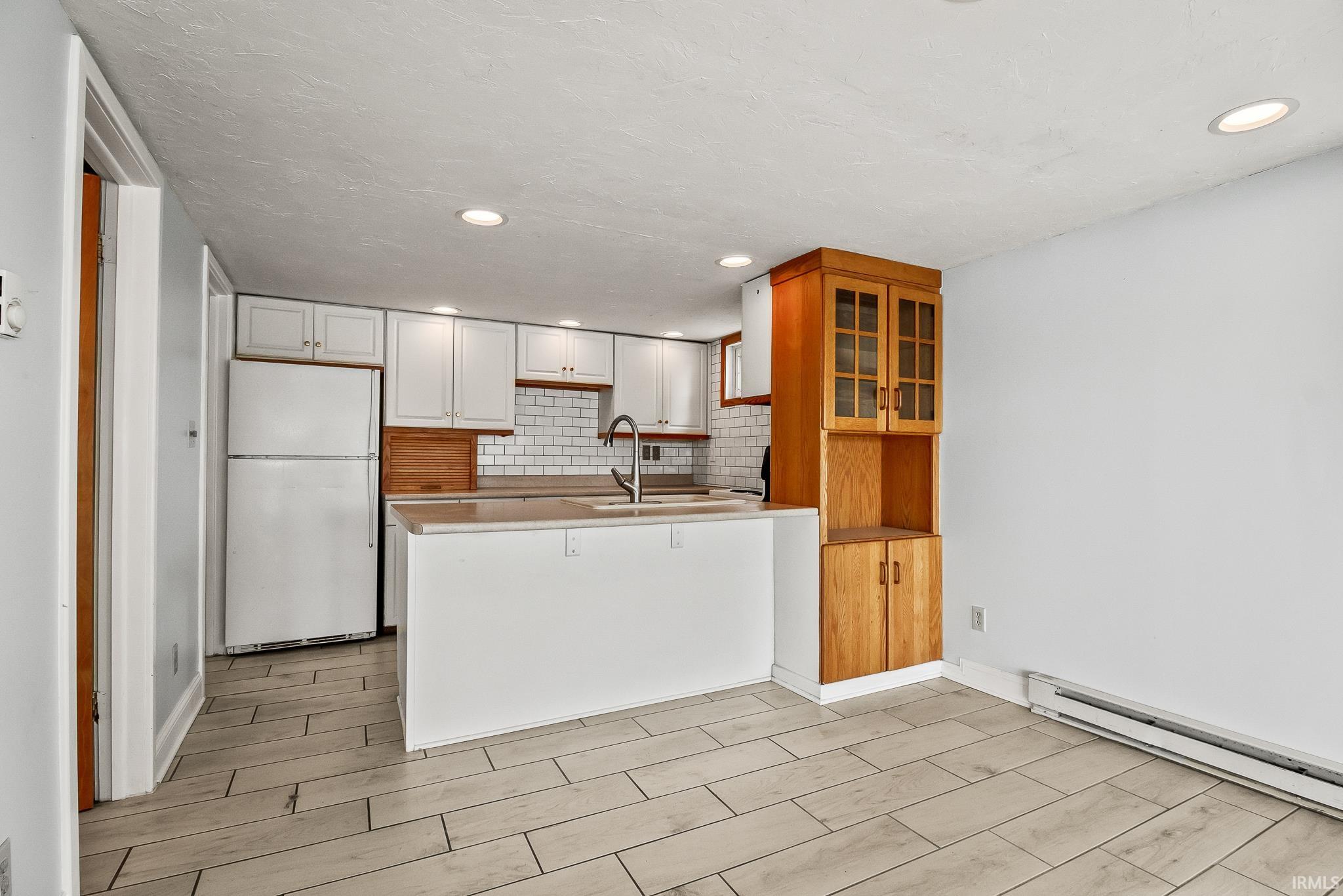Kitchen area featuring white cabinetry, a white subway tile backsplash, and a built-in wooden hutch with glass-fronted upper cabinets
