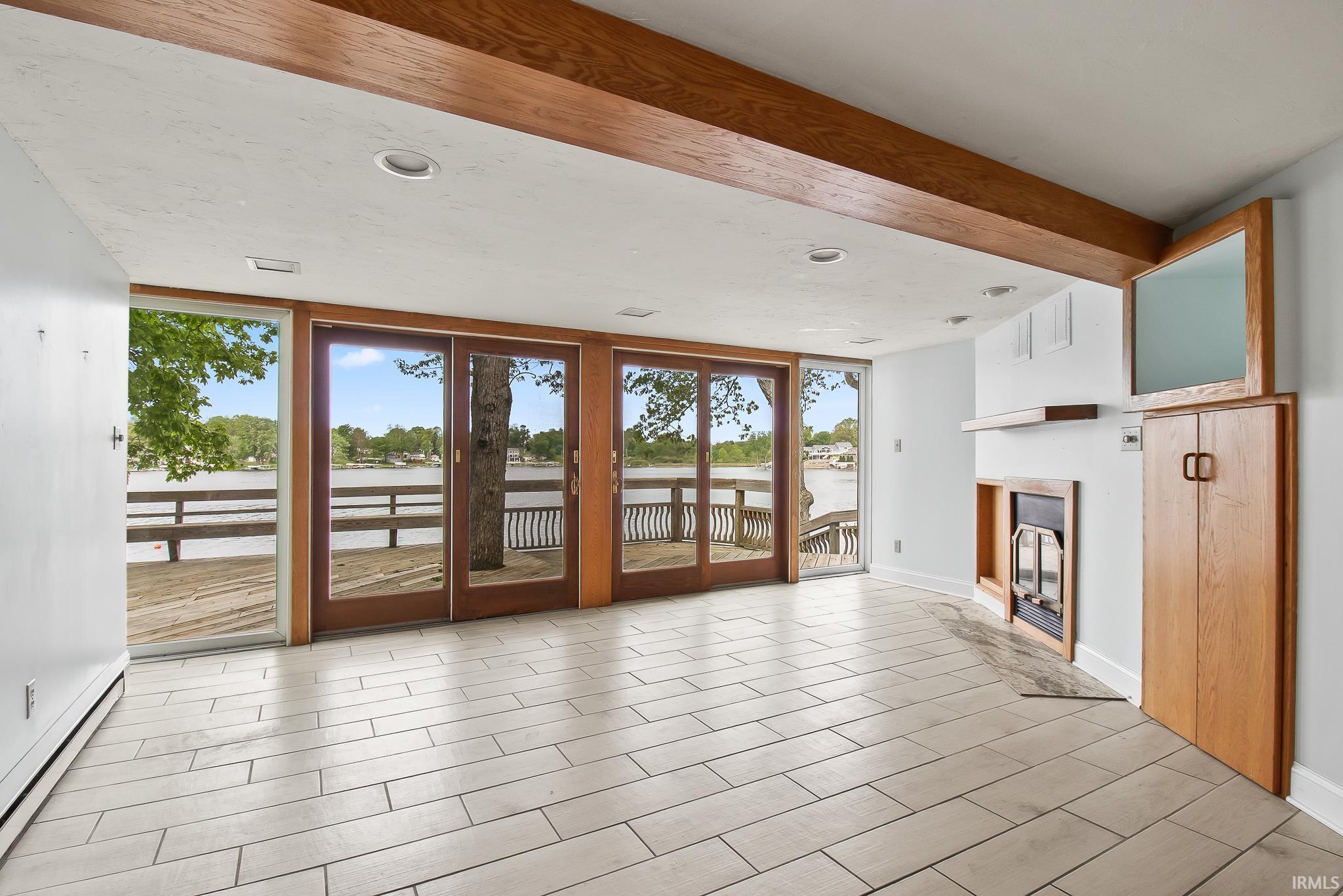 Spacious room featuring multiple full-light wood-frame patio doors, a stone-surround fireplace, built-in cabinetry, exposed wood ceiling beams, and rectangular tile flooring