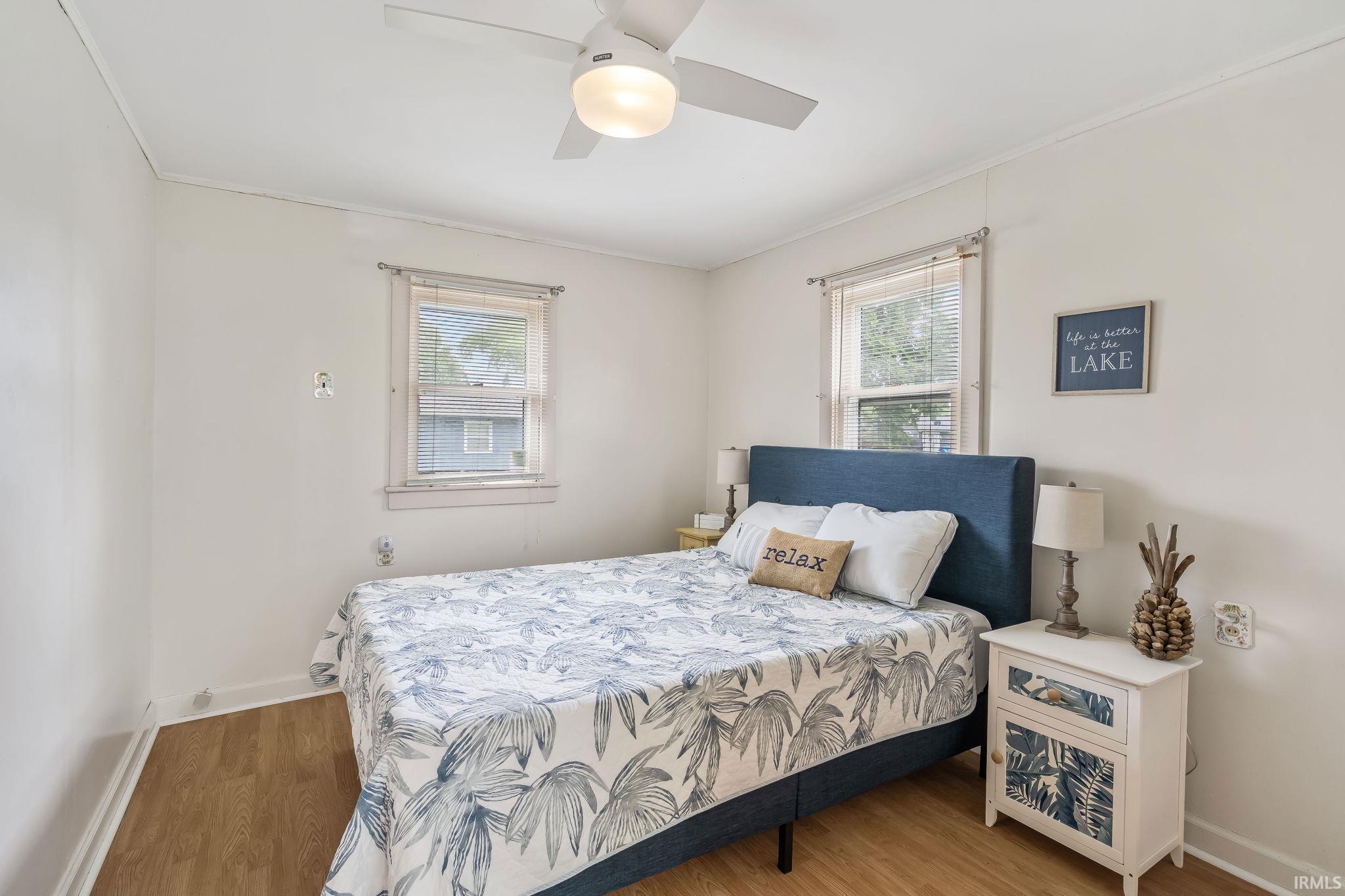Bedroom featuring wood-finish flooring, two sash windows, and a ceiling fan with integrated lighting