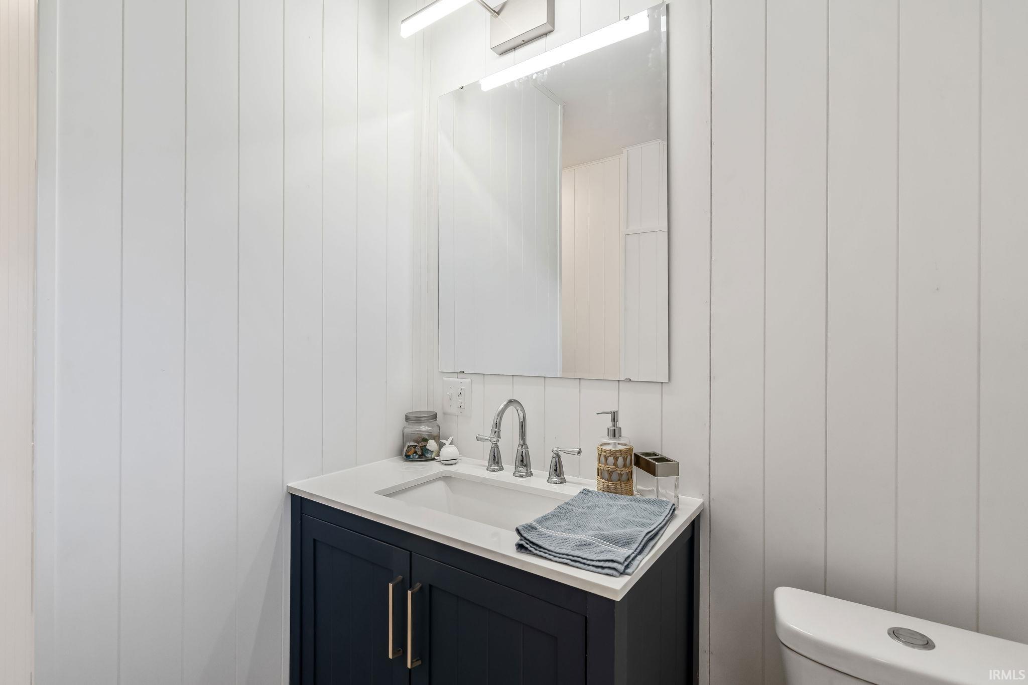 Bathroom vanity featuring a navy blue cabinet with gold-toned hardware, an undermount sink, and a white countertop