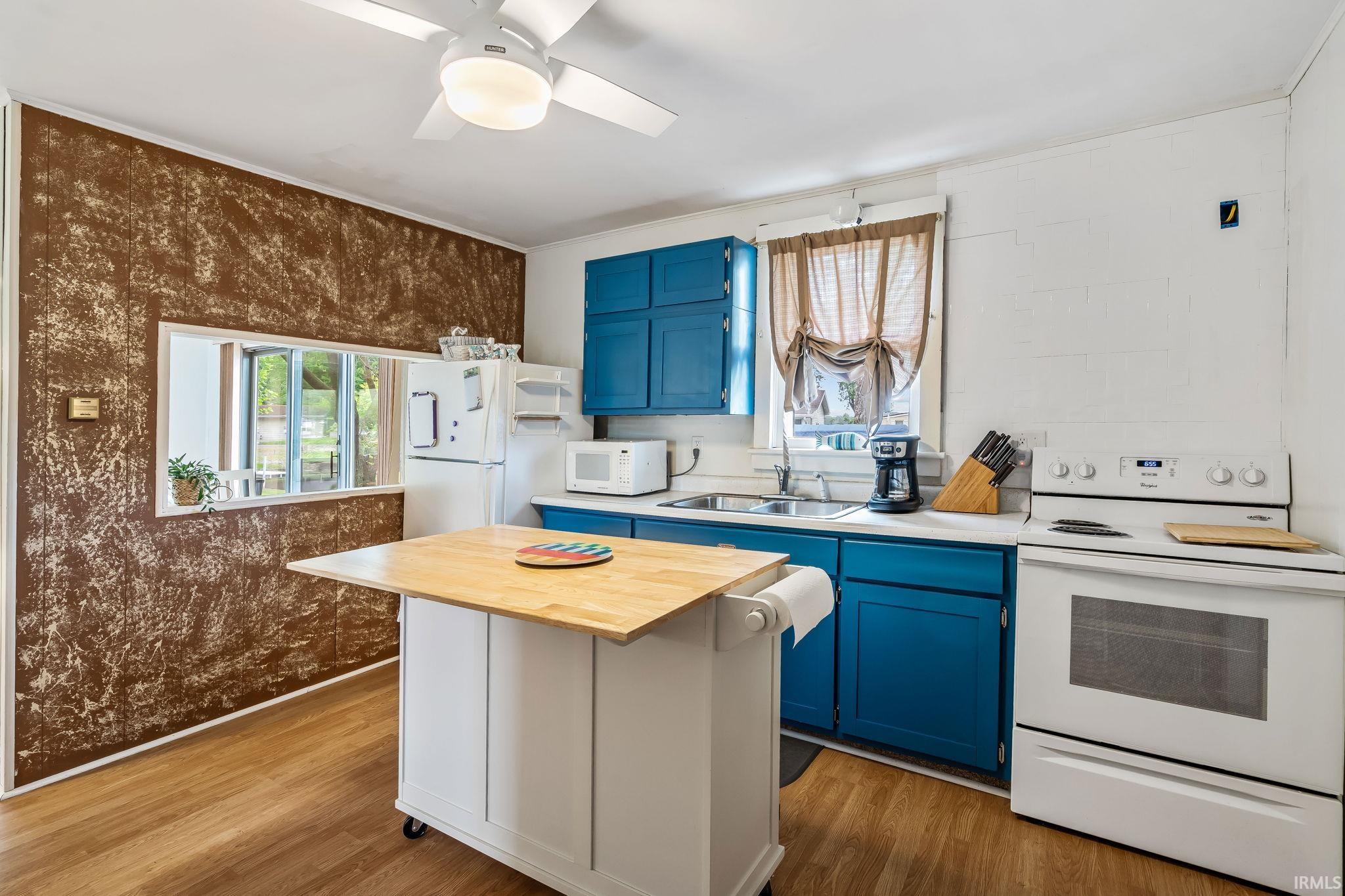 Kitchen space featuring bold blue cabinetry, wood-finish flooring, and white appliances