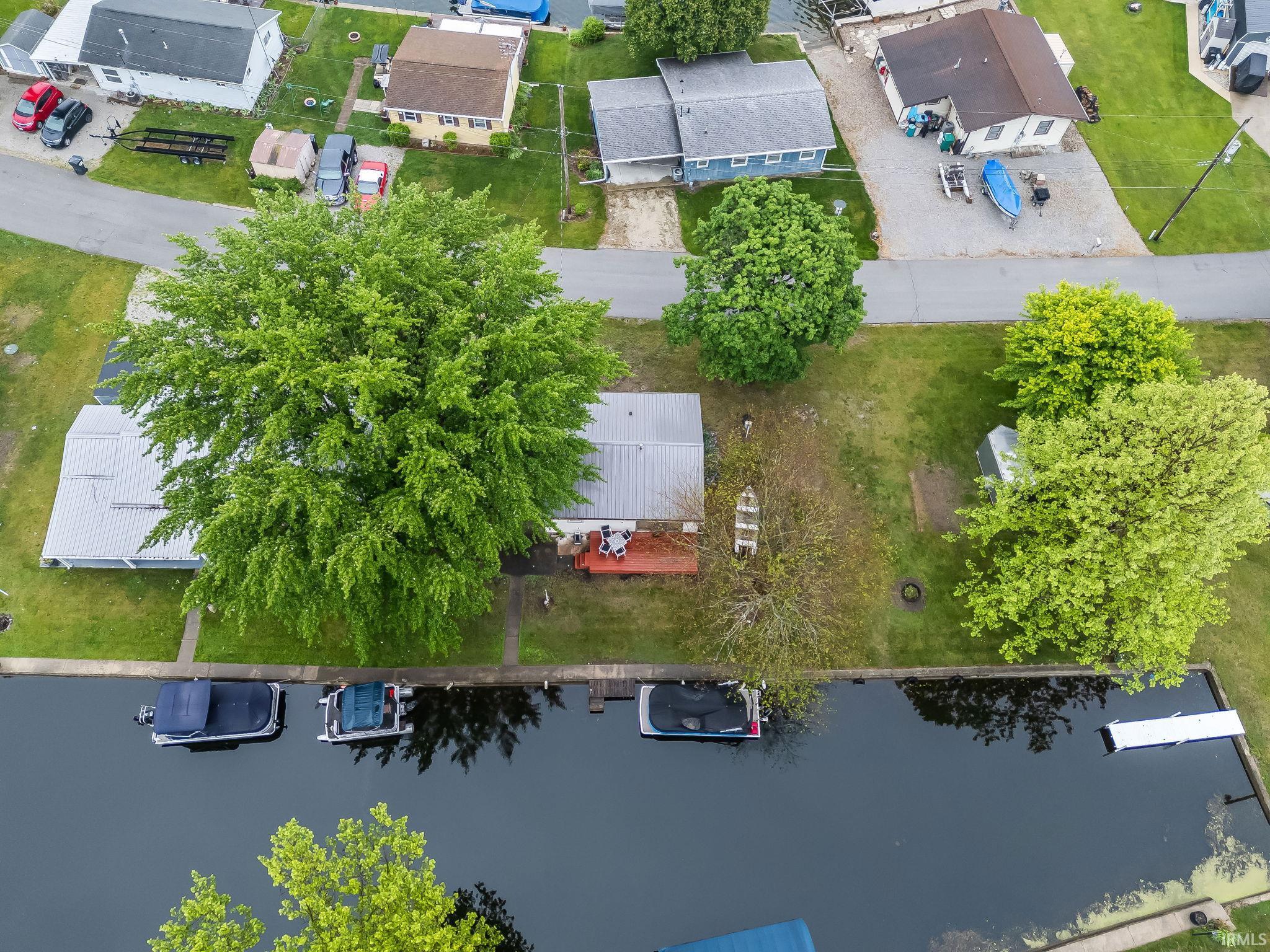 Waterfront property featuring a private boat dock, a wooden patio, mature trees, and a gravel driveway