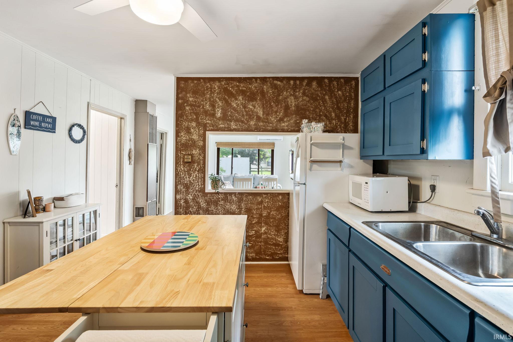 Kitchen featuring a light wood island with built-in storage, contrasting blue cabinetry, a stainless steel double basin sink, and wood-finish flooring
