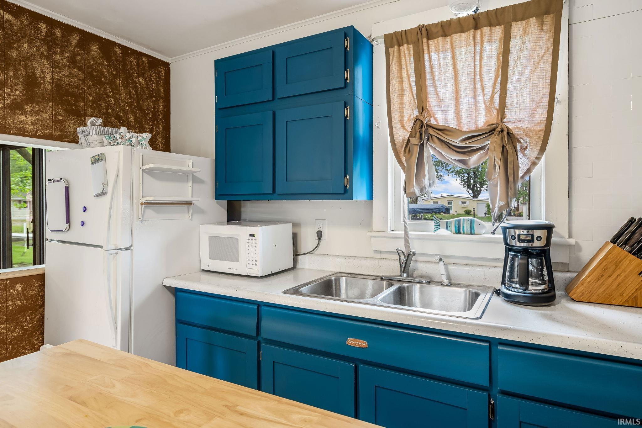 Kitchen featuring bold blue cabinetry, white countertops, a double basin stainless steel sink, and a large window