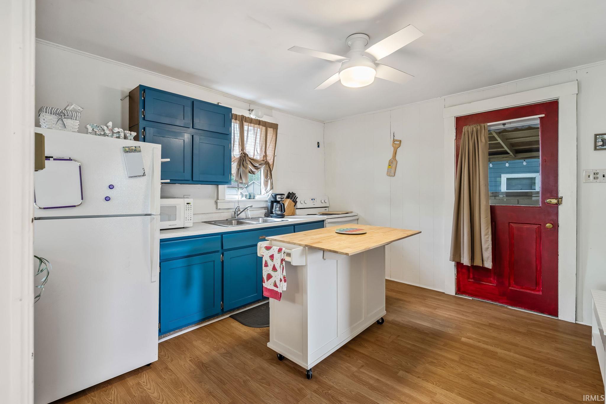 Kitchen featuring wood-finish flooring, white paneled walls, and a ceiling fan with integrated lighting