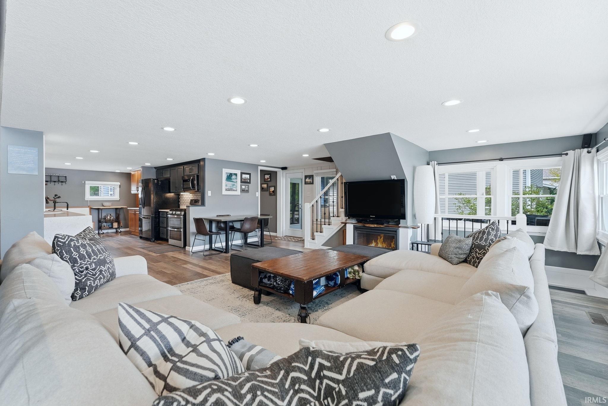 Open-concept living space featuring wood-finish flooring, recessed lighting, and a modern fireplace with integrated media area